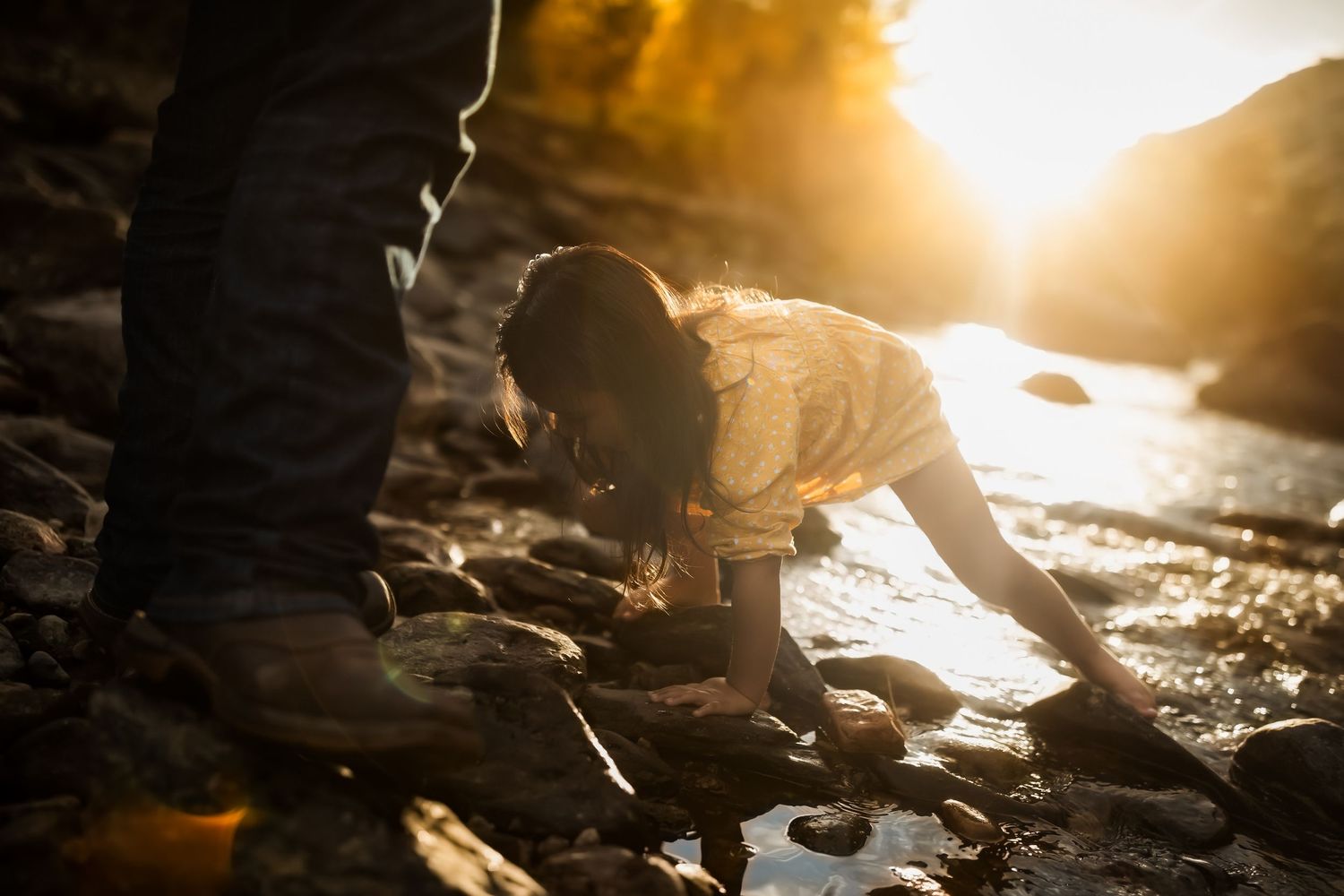 Silhouette of people exploring rocky shore during golden hour sunset.