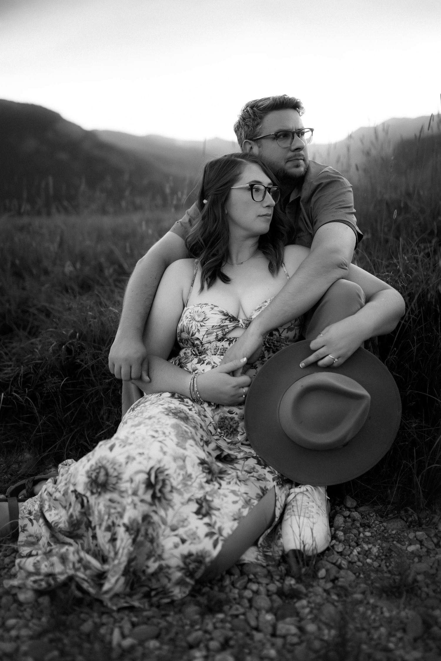 A couple relaxes together on rocky ground during a black and white outdoor photo session.