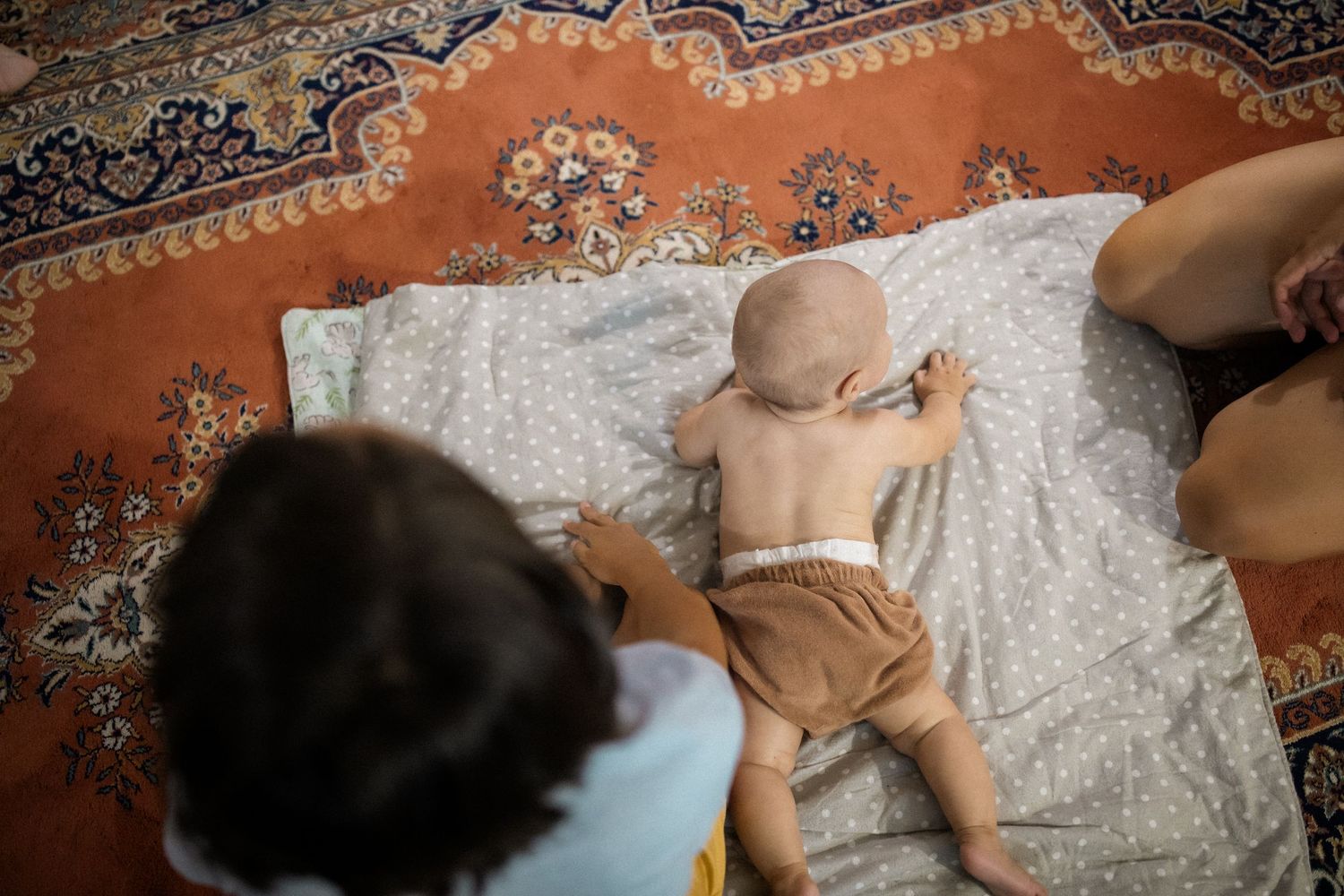 A baby lies on a patterned carpet while reaching up to play with a toy during tummy time.