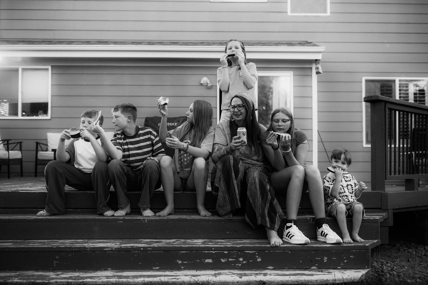 Black and white photo of children sitting on porch steps enjoying ice cream together at dusk.