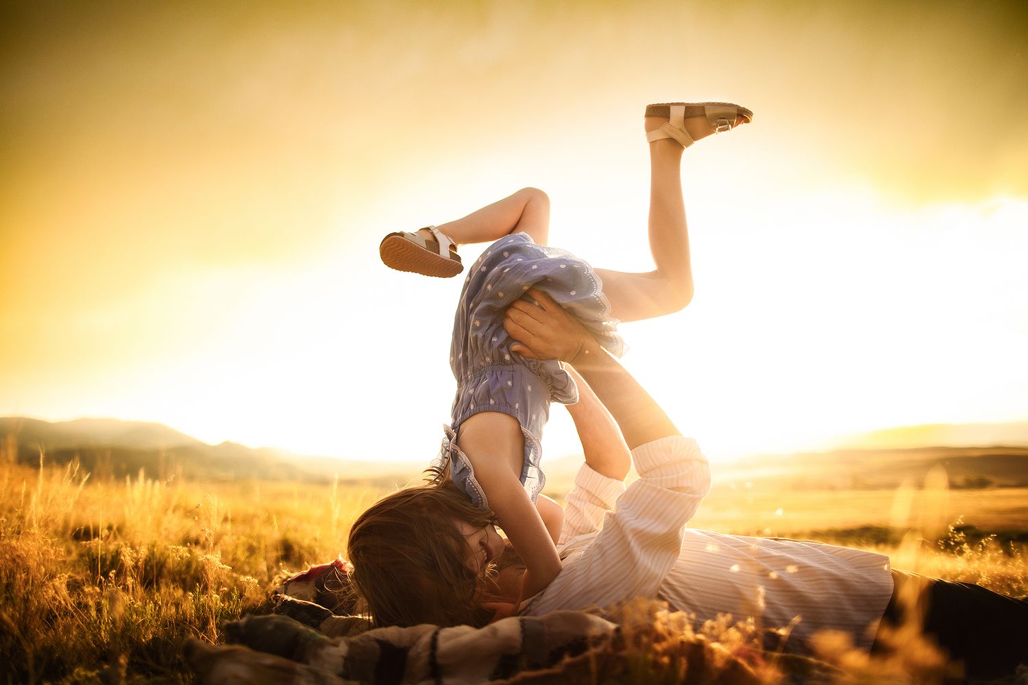 Playful couple silhouetted against golden sunset in field.