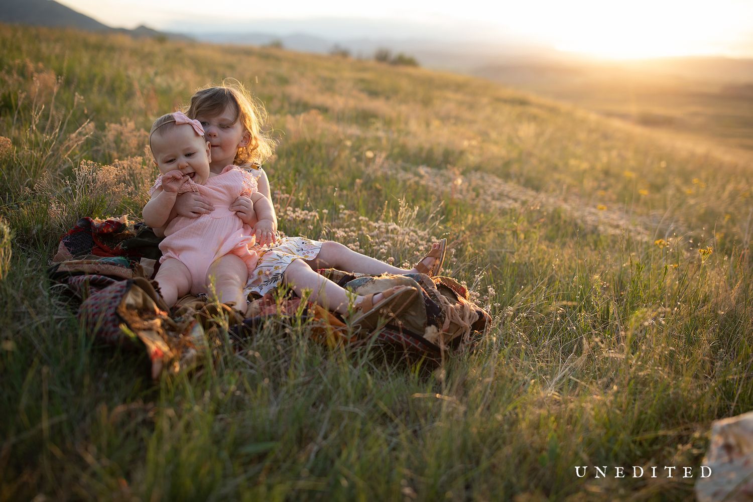 Family relaxing together in sunlit meadow during golden hour.