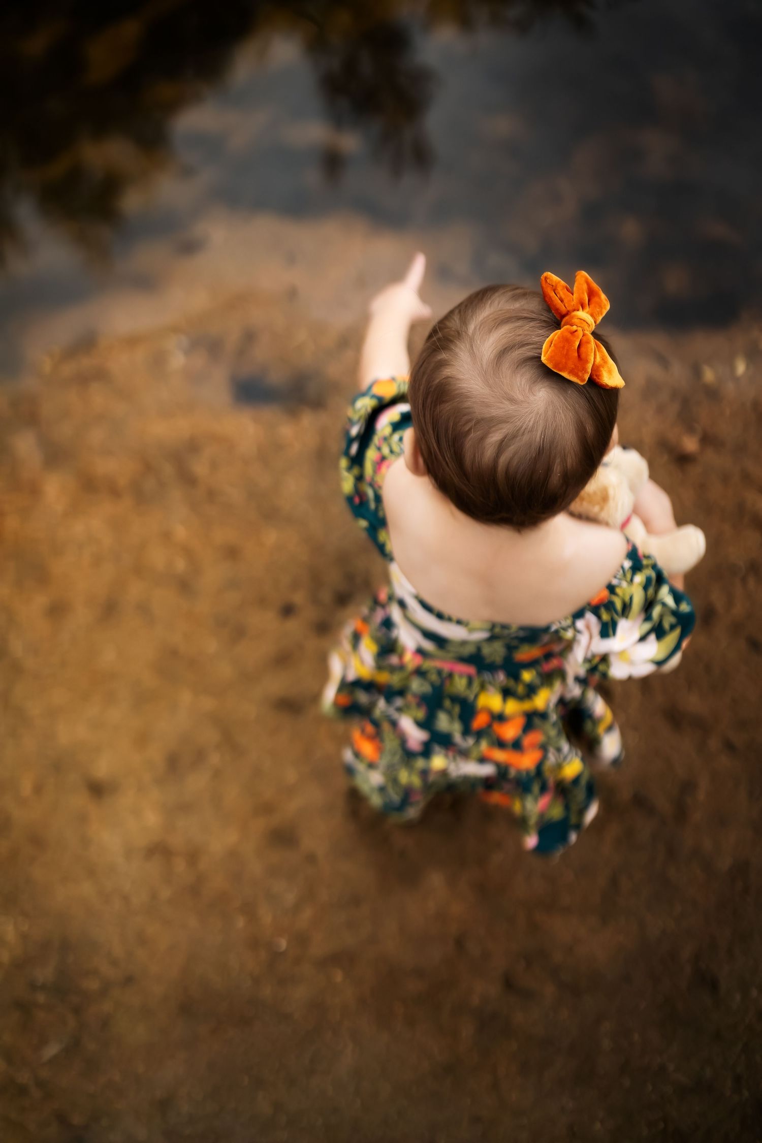 A bird's eye view of a small child wearing a floral dress with an orange bow in their hair.