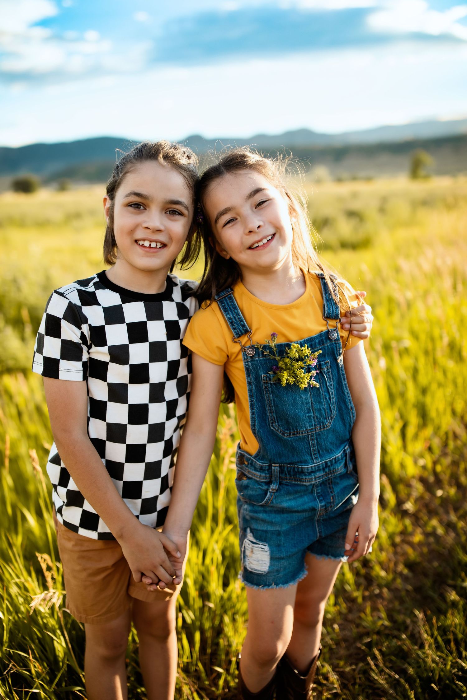 Two children in casual clothes playing in a sunlit field of tall grass.