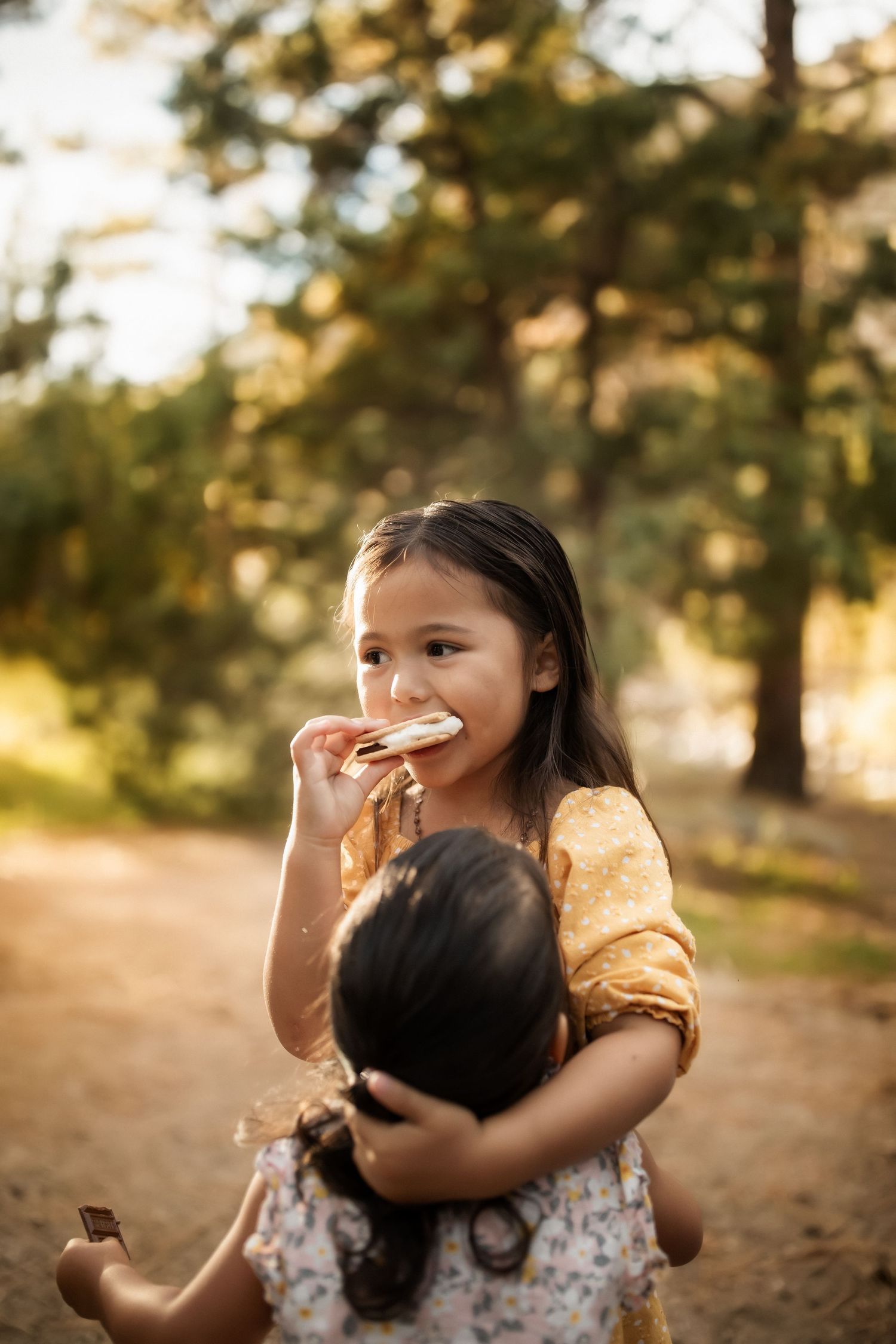 Child playing and laughing while wearing a yellow and floral outfit in a forest setting.