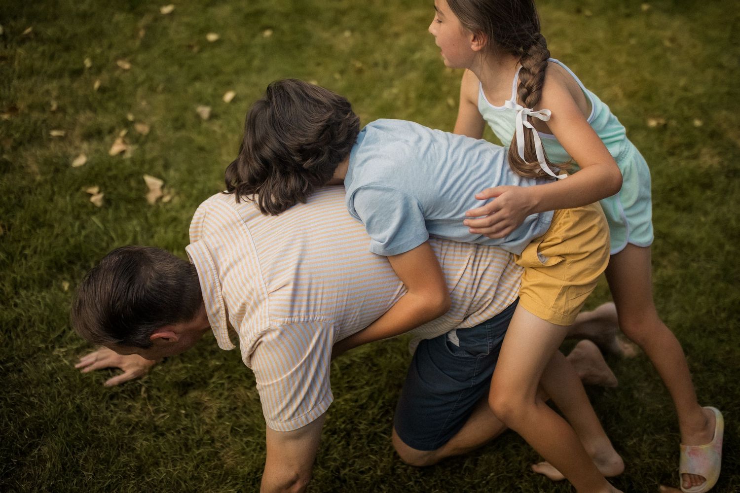 A sequence of seven photos showing people playing and rolling on grass in a playful manner outdoors.