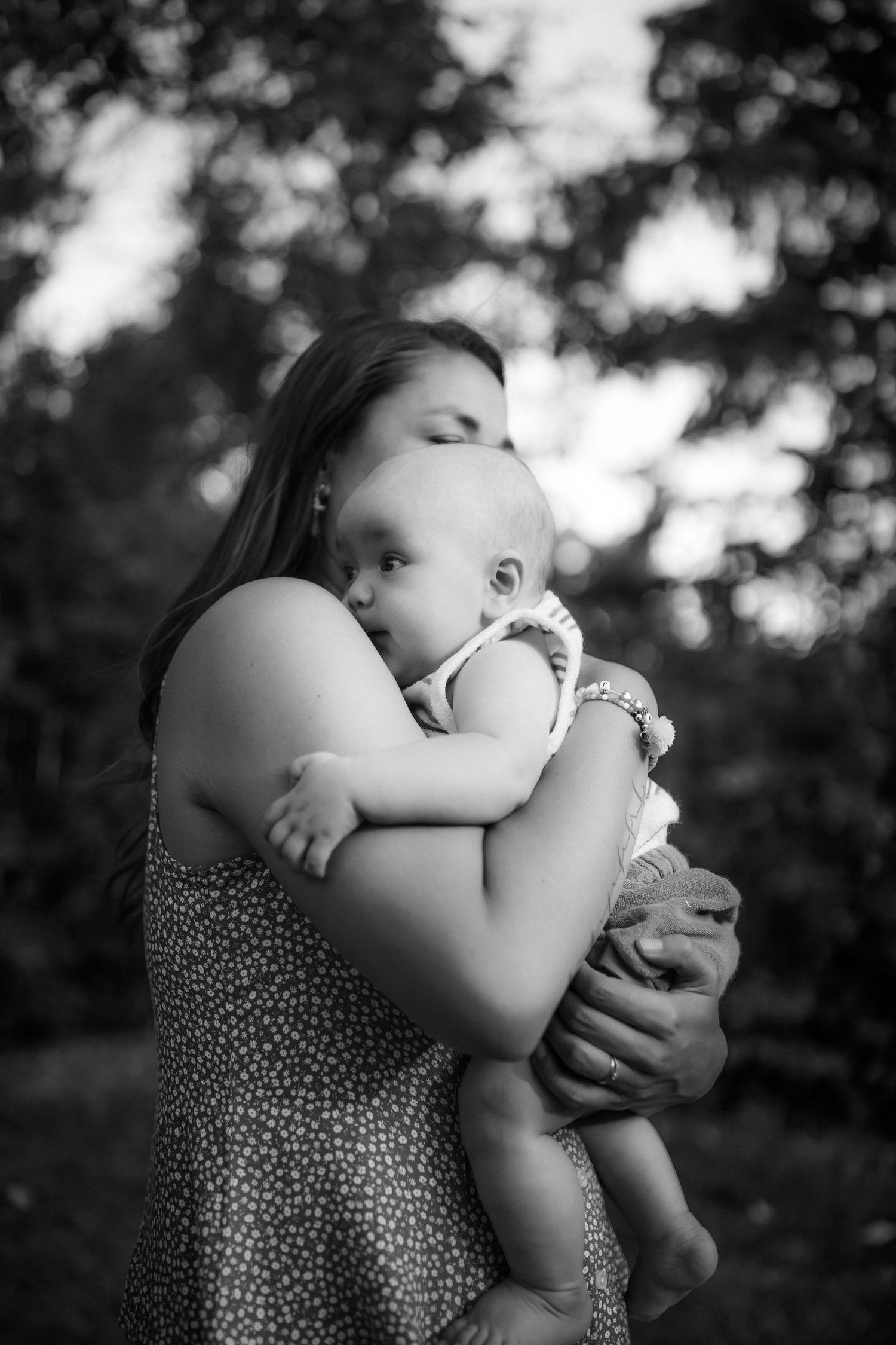A tender black and white portrait of a parent embracing their infant child against a blurred outdoor background.