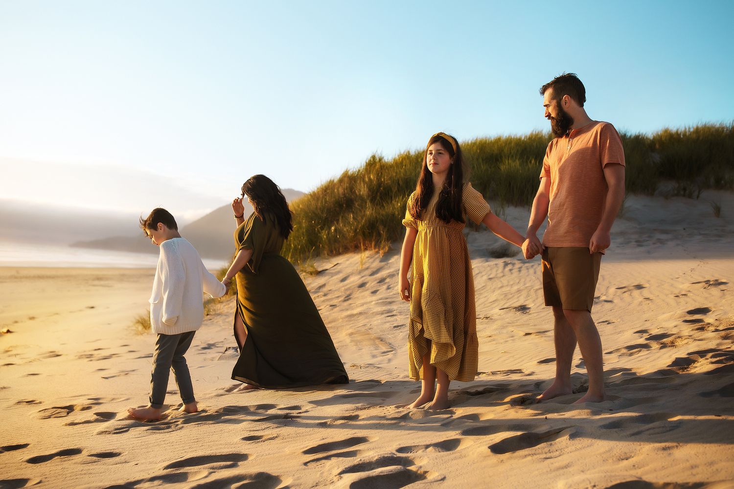 Family walking along beach shoreline at sunset.
