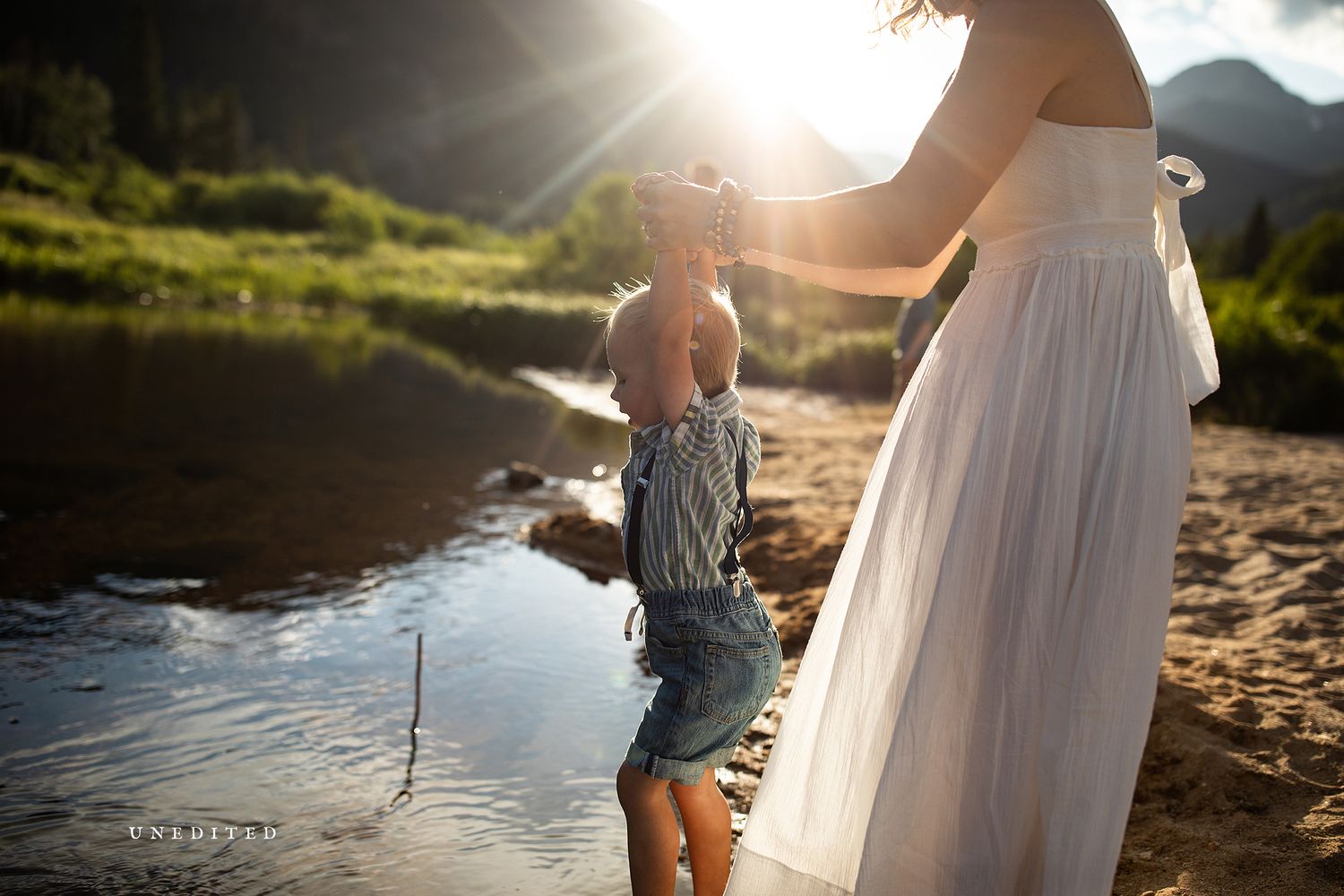 Couple walking along a sunlit riverbank during golden hour creating romantic silhouettes.