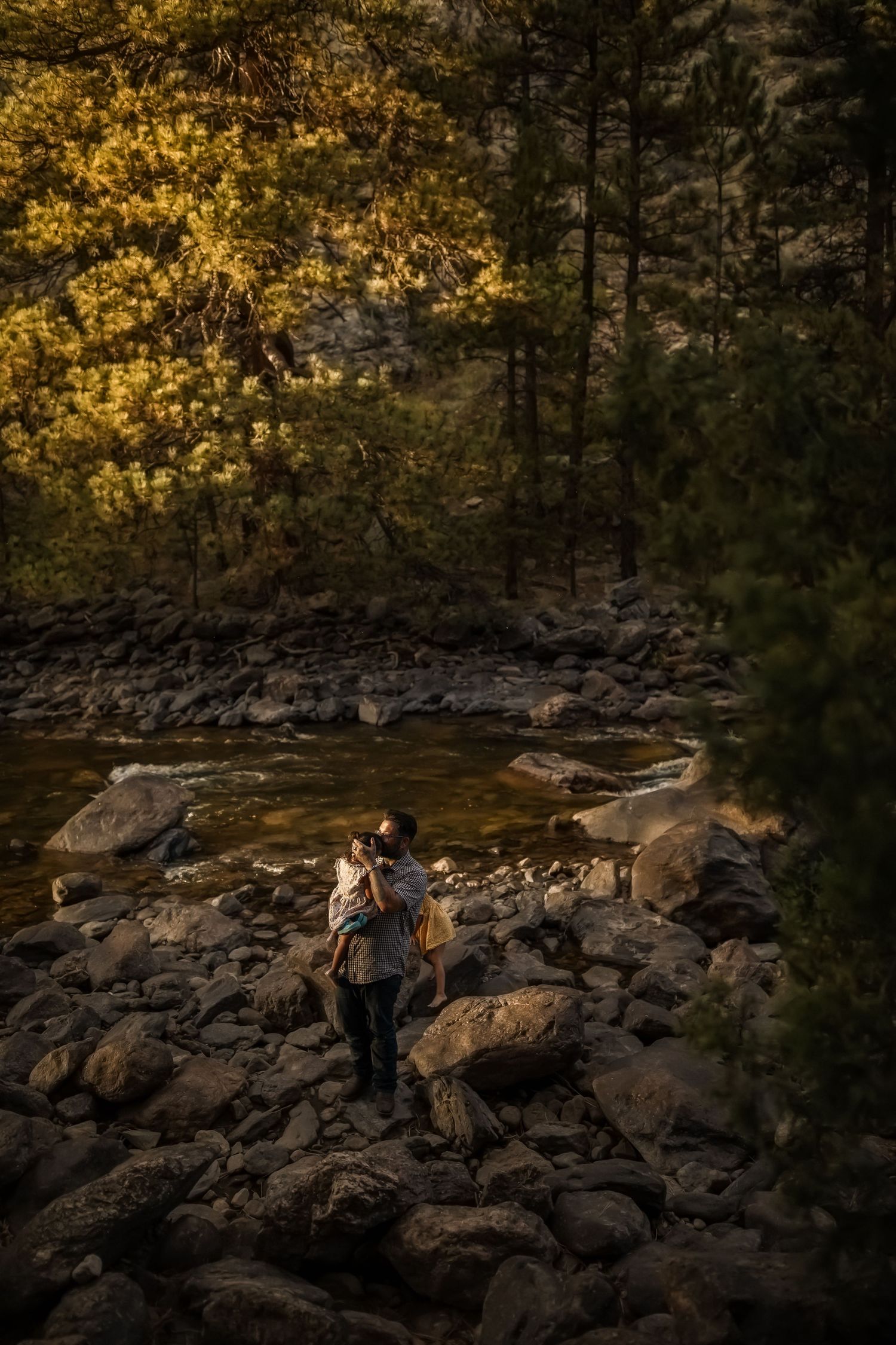 Family walking together on rocky terrain during sunset in a pine forest.
