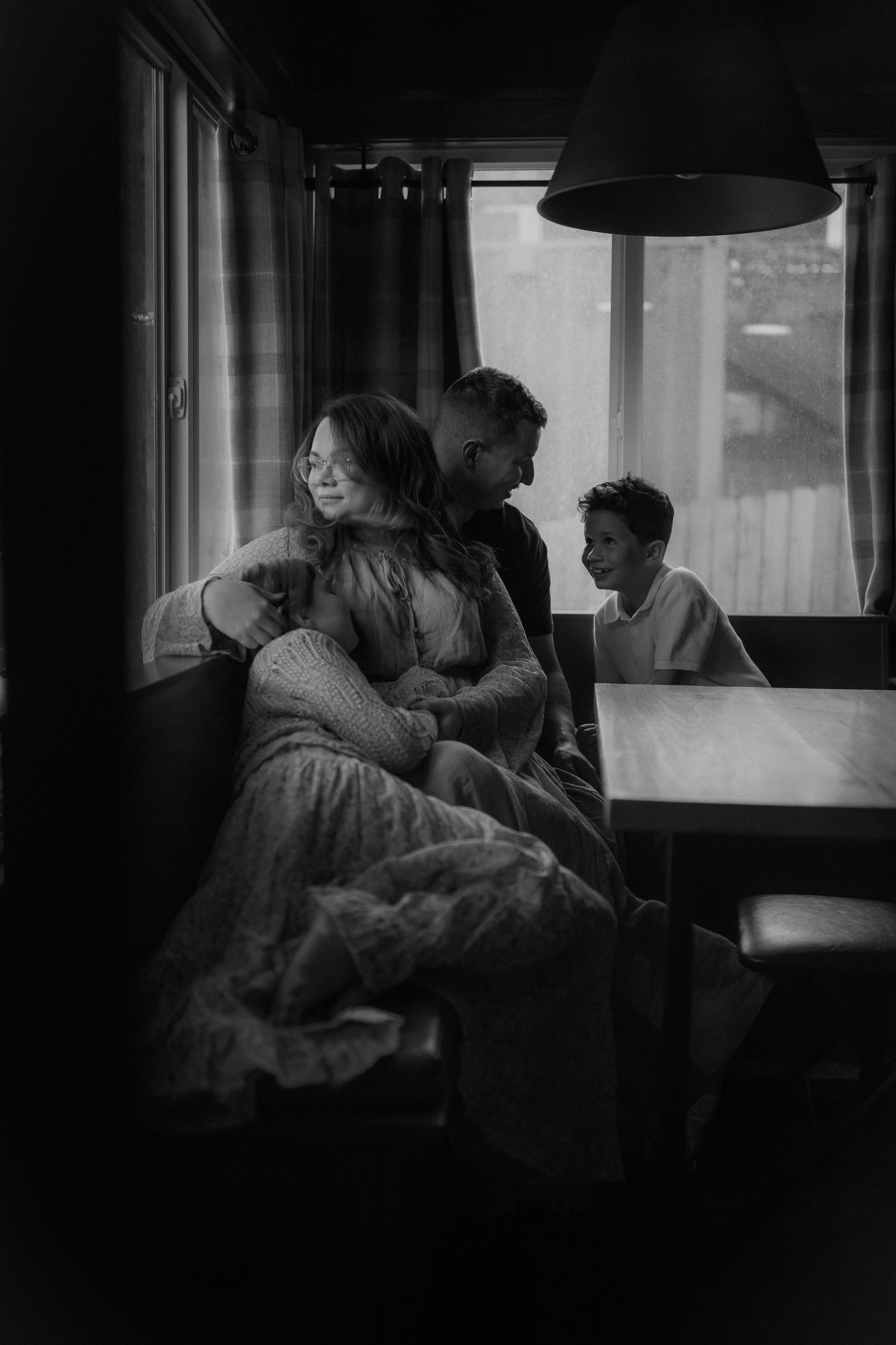 Black and white photo of a family sharing a warm embrace indoors, with a child smiling in the background.