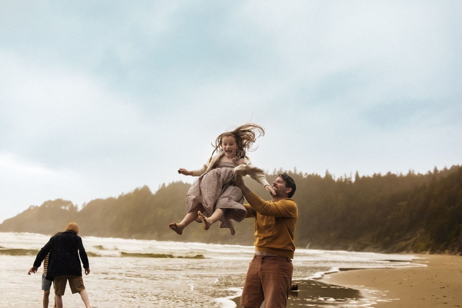 A couple shares a joyful moment on a misty beach as one person lifts the other in a playful spin at sunset.