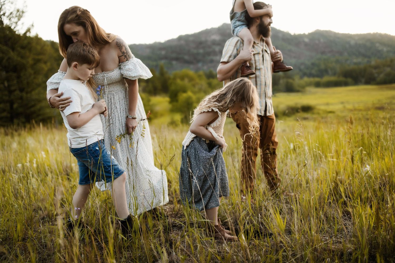 A family of four walking through a grassy field with mountains in the background.