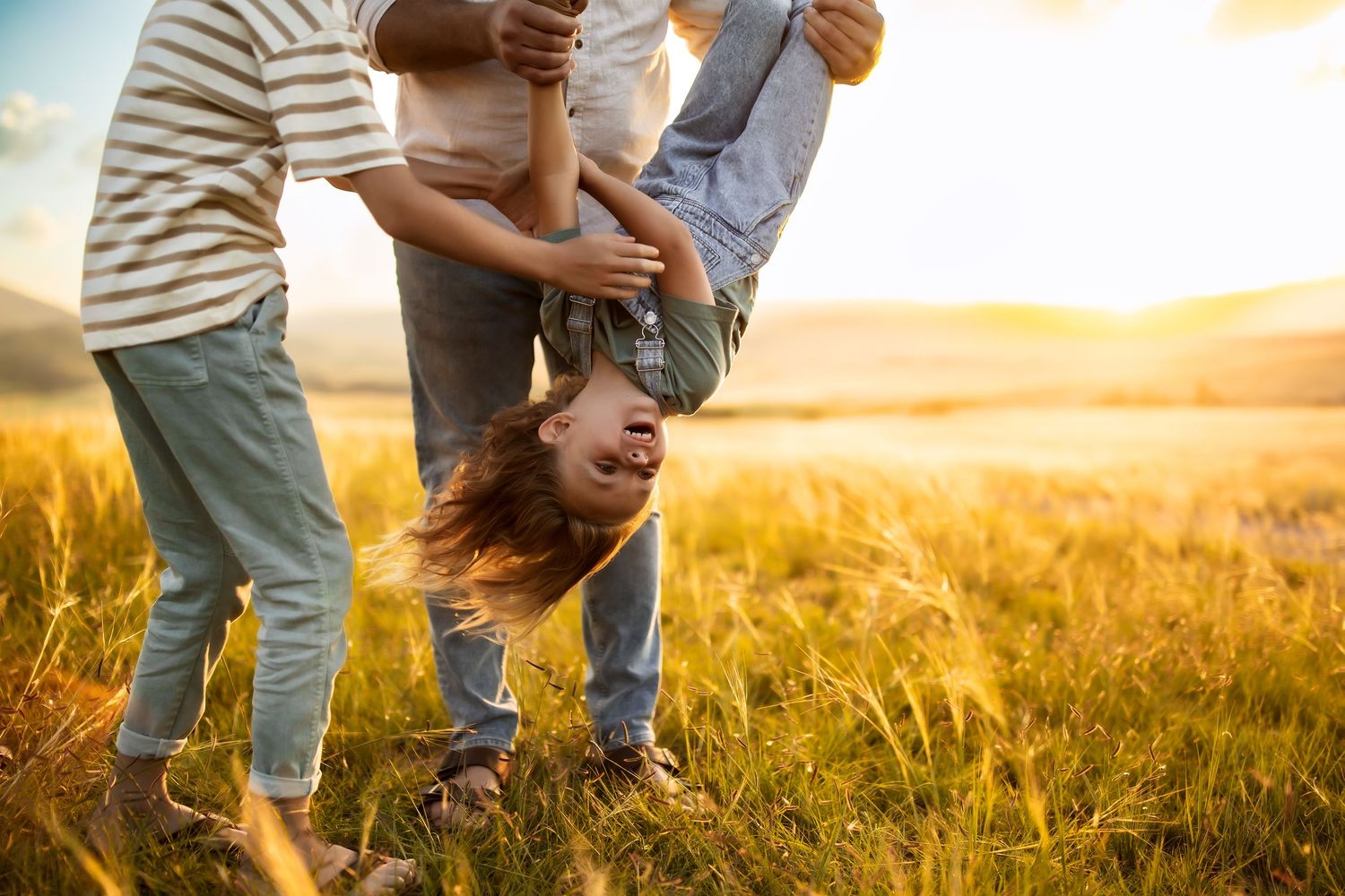 Family embracing in golden wheat field at sunset with warm sunlight glowing through their silhouettes.