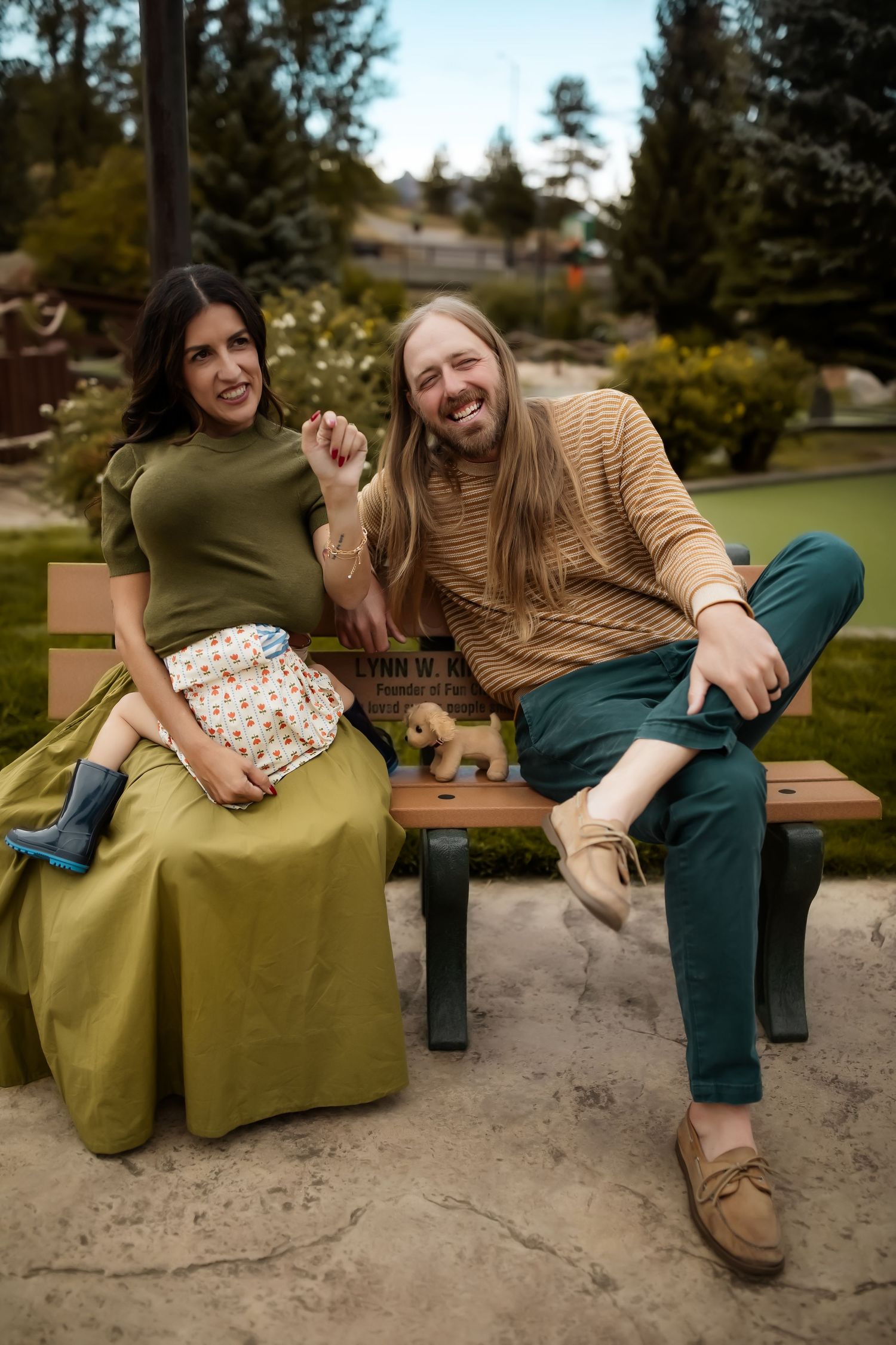 Two people relaxing on green cushioned bench in park setting.