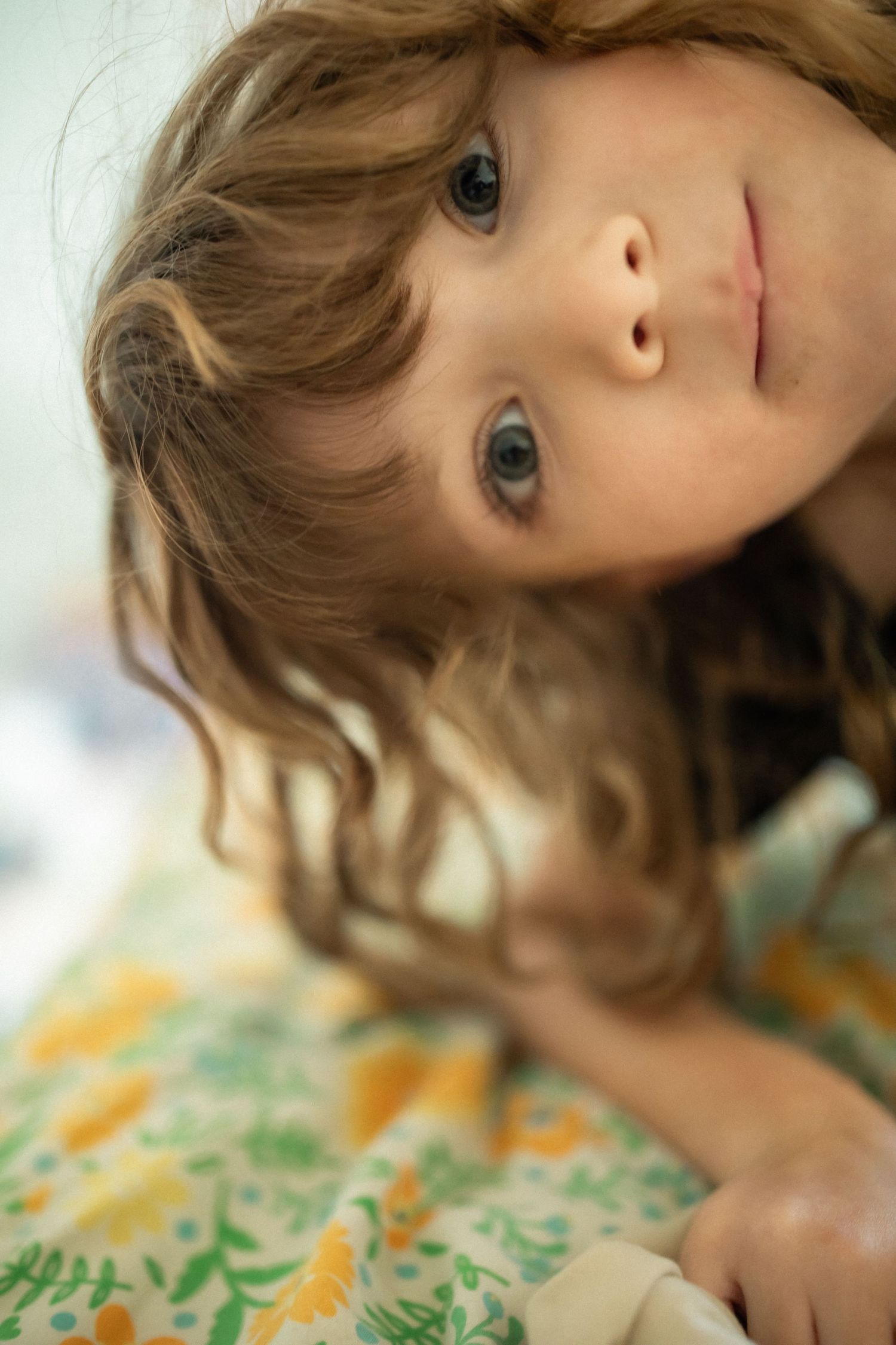 Close-up portrait of young child with curly hair lying on floral fabric.