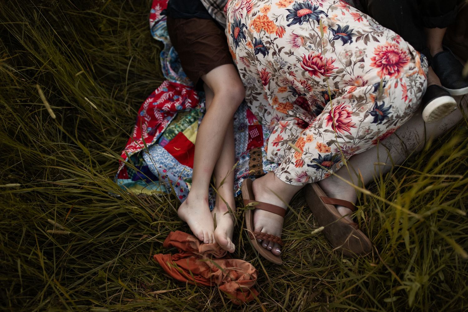 Romantic couple lying in tall grass wearing floral dress during sunset photoshoot.