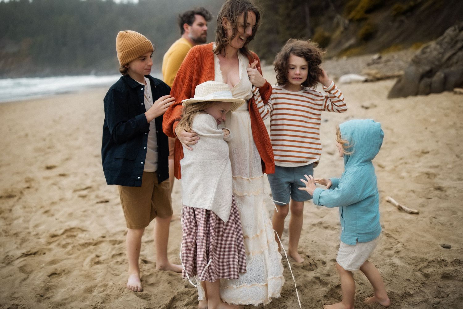 A family enjoys a casual stroll together on a misty beach wearing cozy sweaters and casual attire.