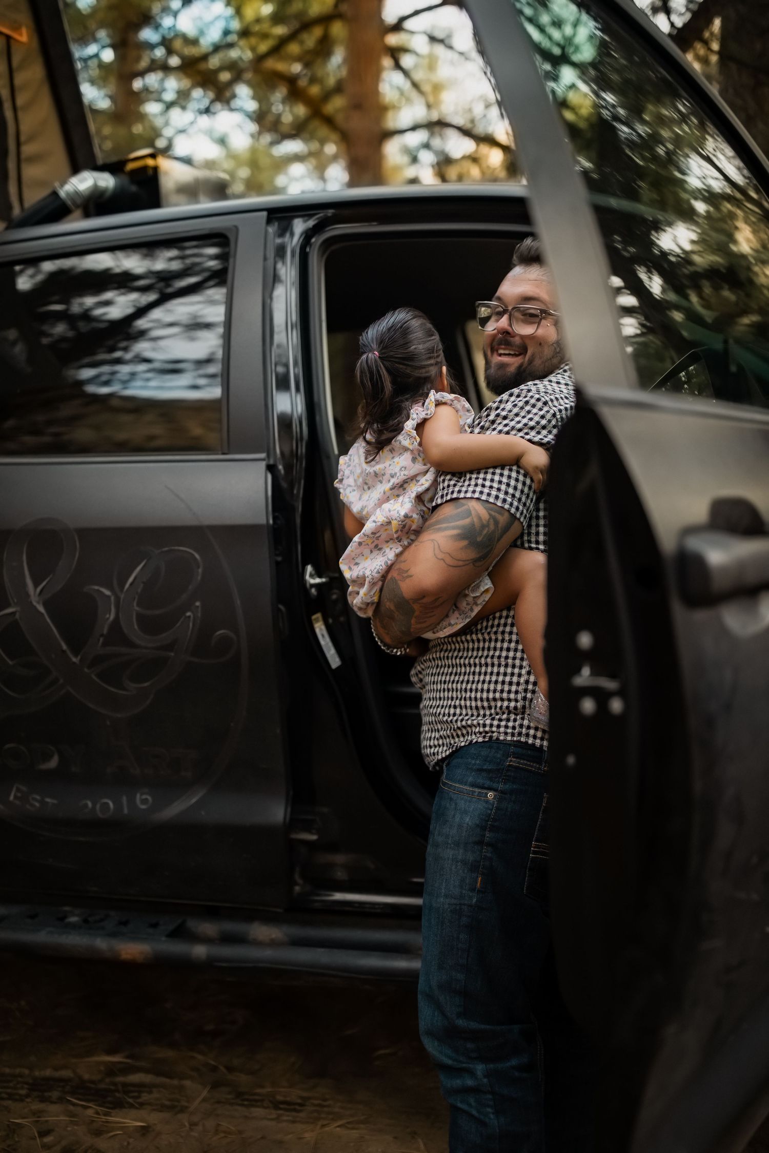 A series of intimate photos by a vintage black car showing a sweet embrace in natural lighting.