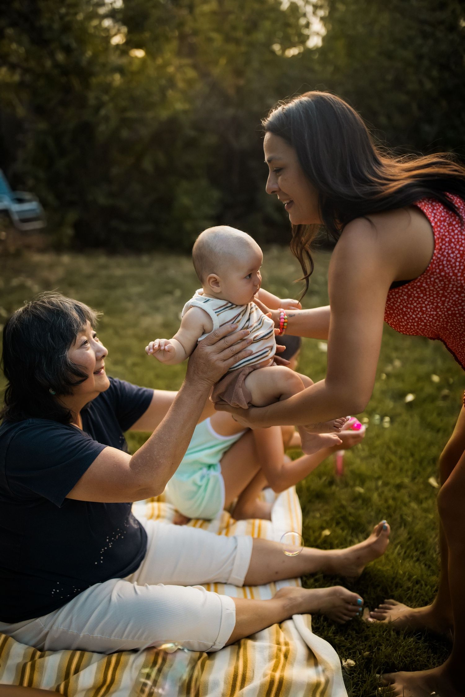 Family enjoying a tender moment together on a blanket in a sunlit backyard during golden hour.