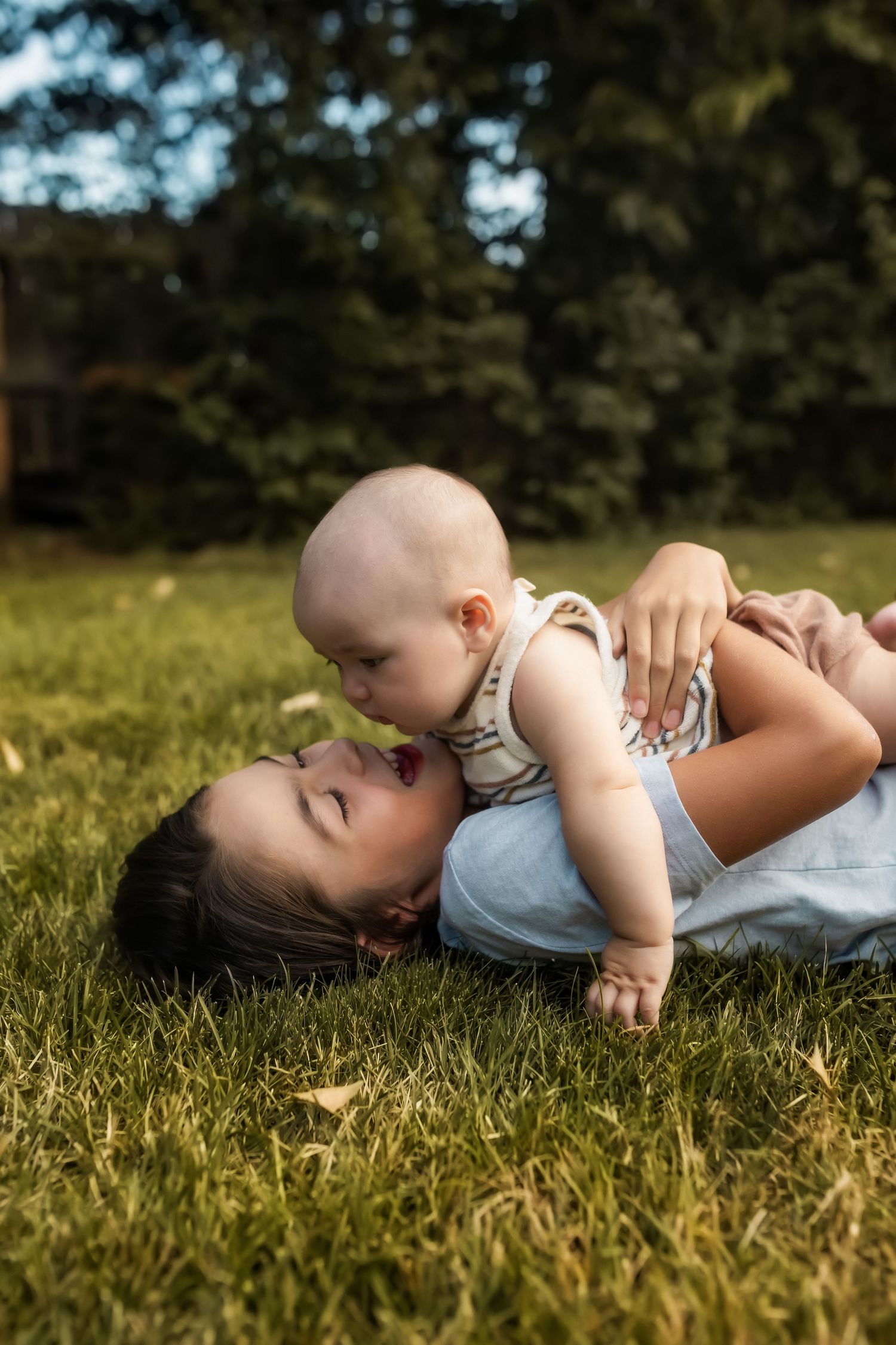 A tender moment captured as parent and baby lie together on green grass in warm sunlight.