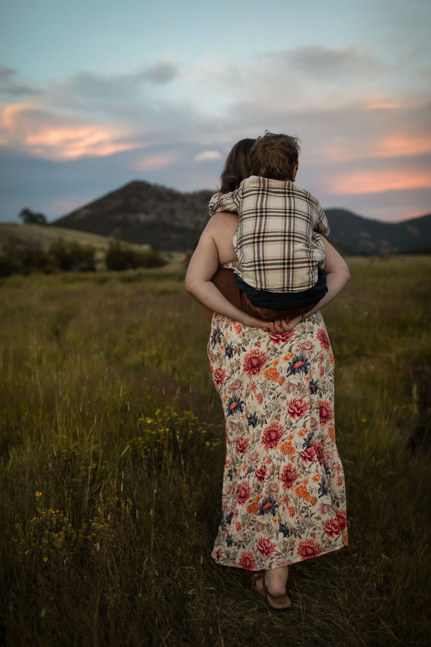 A tender embrace captured in a wildflower meadow with mountains silhouetted at dusk.
