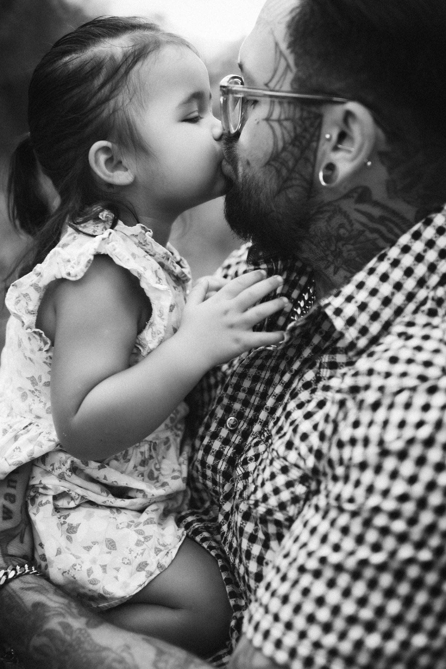 Tender moment between child in floral dress and bearded person in checkered shirt.