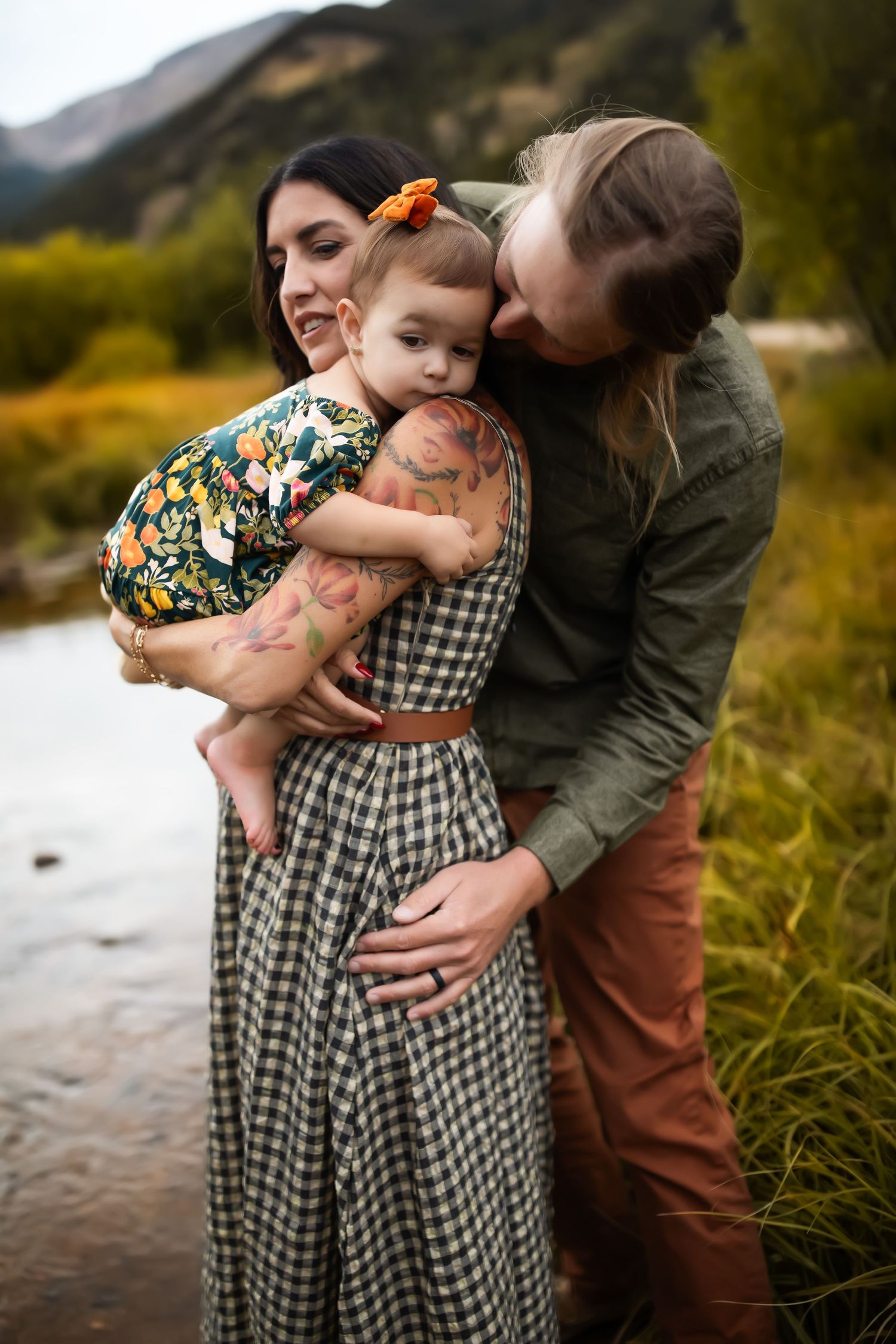 A family embraces outdoors with mountains and autumn foliage in the background.
