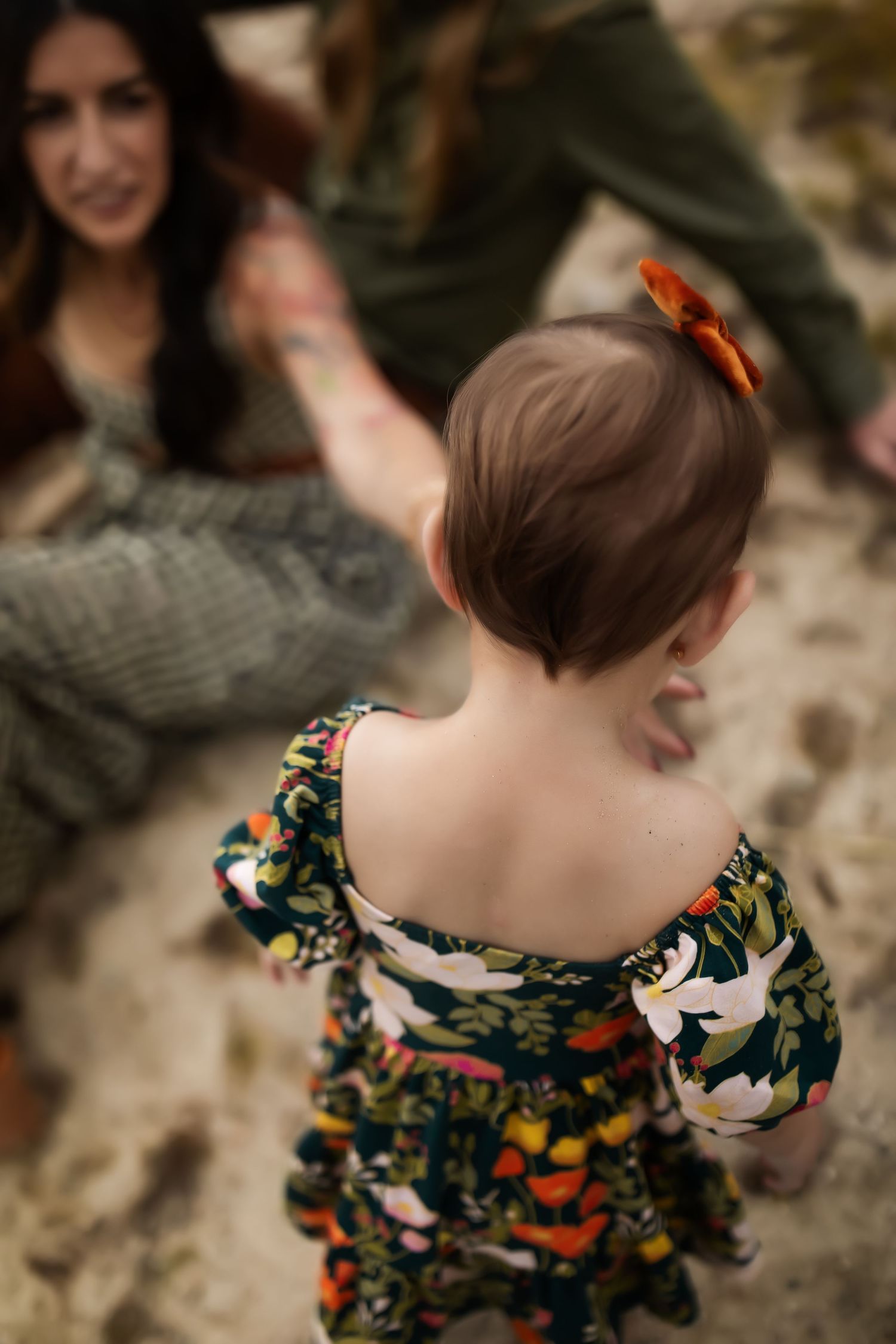 Child wearing colorful floral dress plays near water's edge on rocky shore.