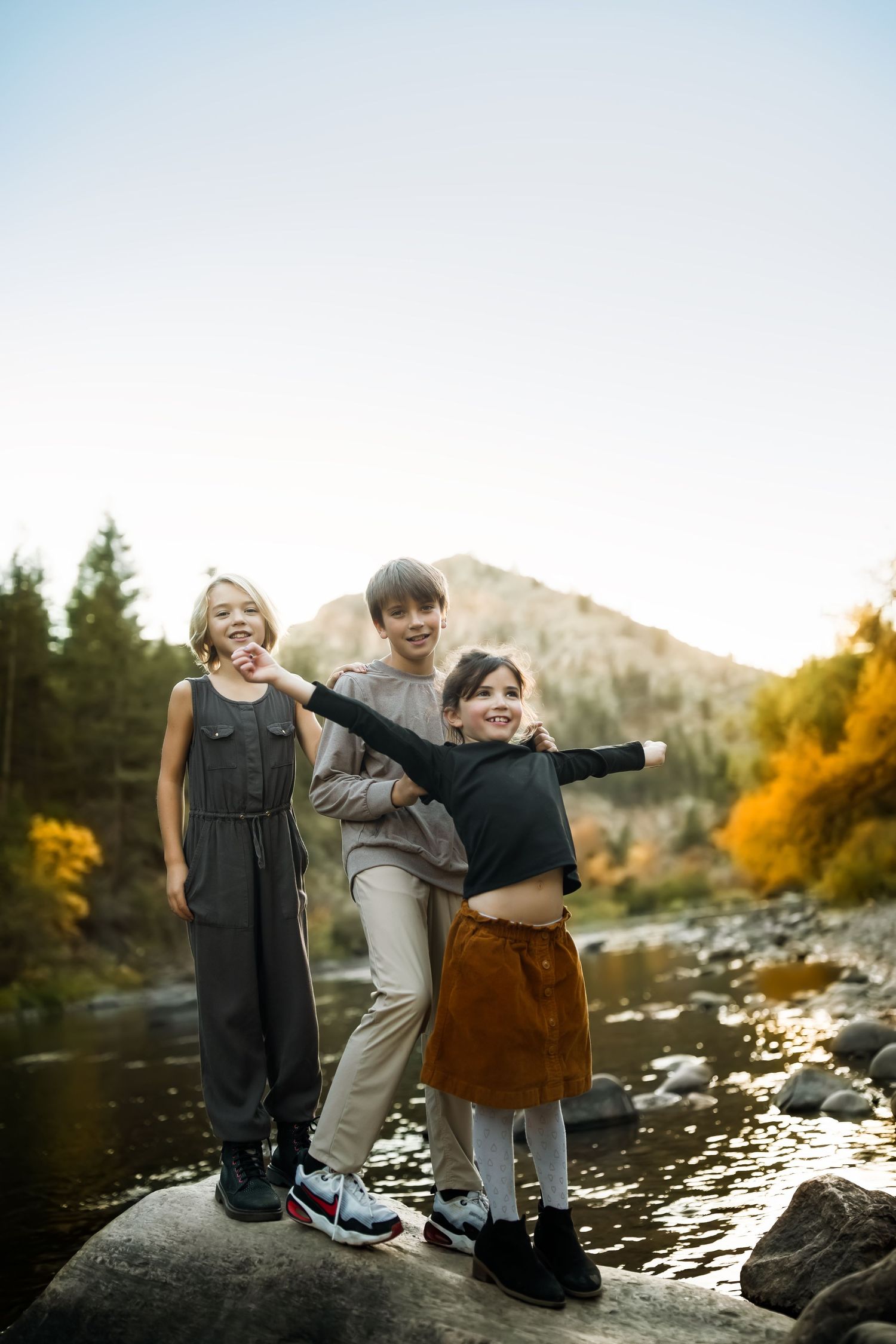 Three people standing on large rocks by a mountain stream at sunset.