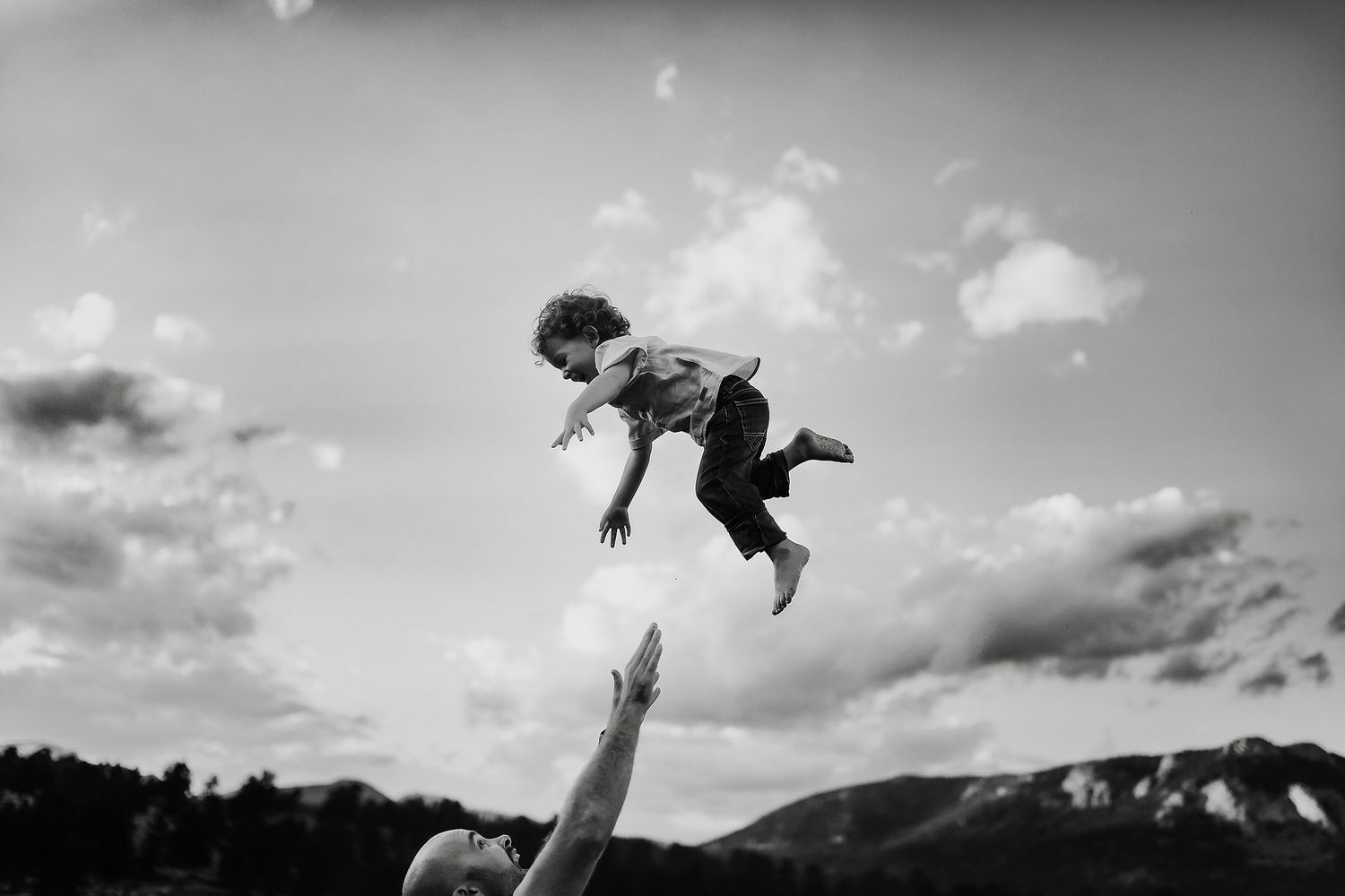 People leap and play in silhouette against a dramatic cloudy sky.