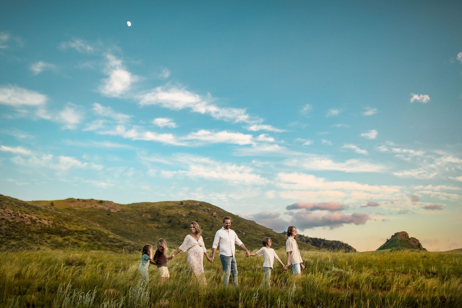 Group walking through a scenic mountain meadow under bright blue skies with puffy white clouds.