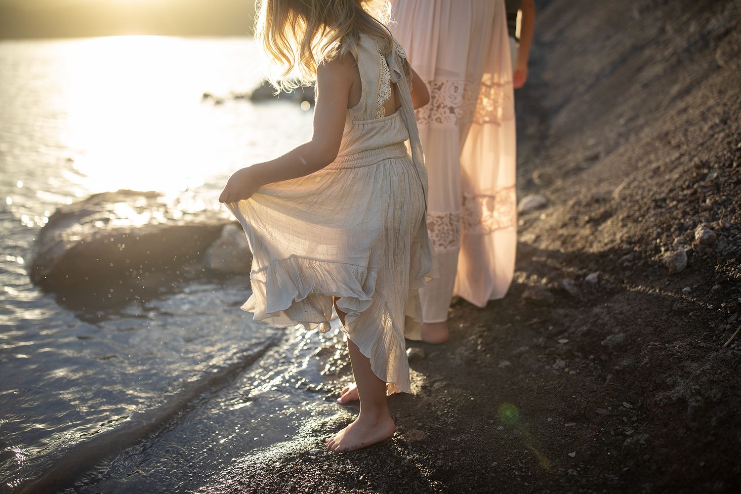 Sunlight filters through figures walking along a rocky beach at sunset.