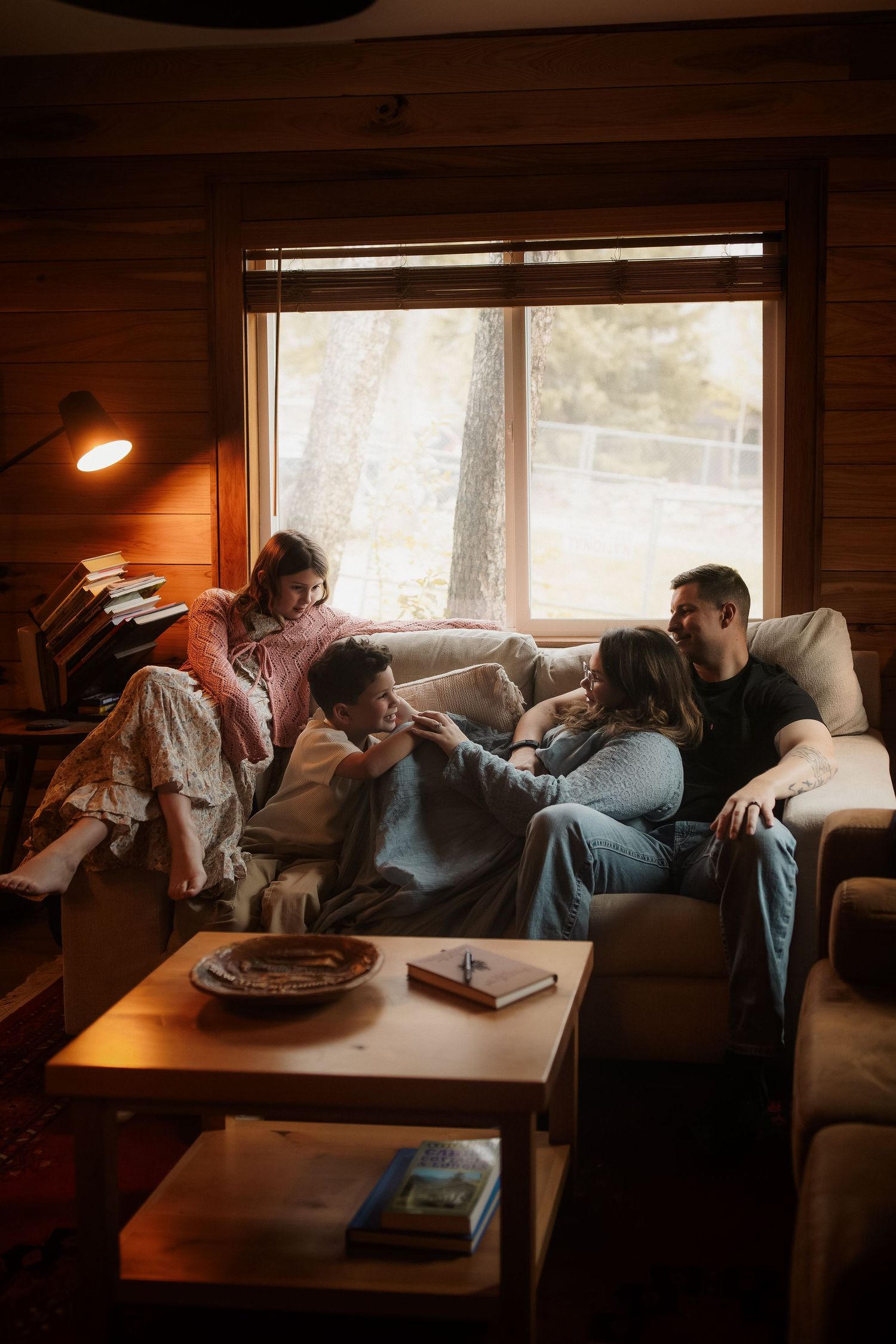 Family relaxing together on a cozy cabin sofa near a large window with warm lamp light.