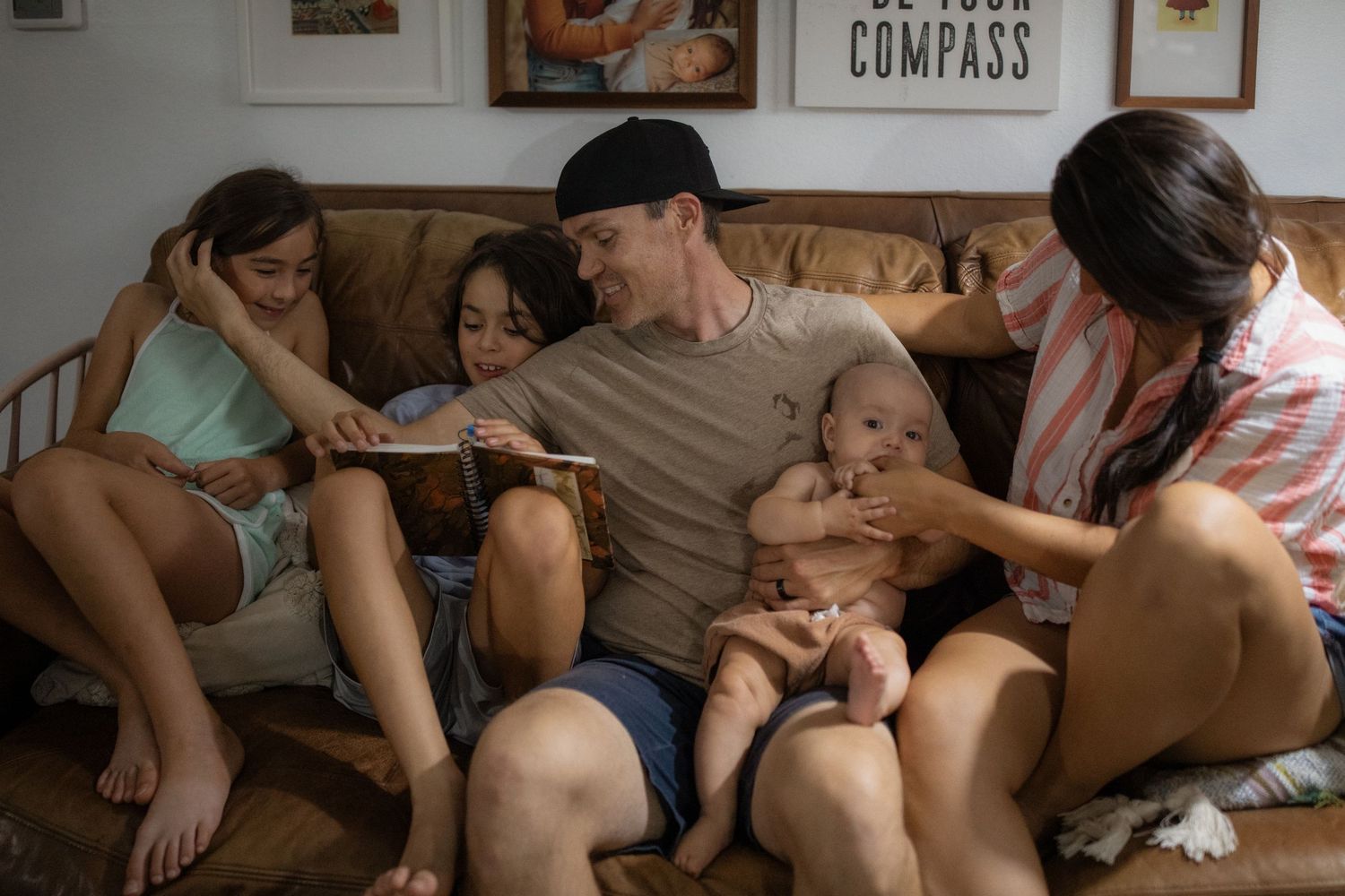 Family relaxing together on a couch, with a man holding a baby surrounded by children and a woman in a cozy living room.