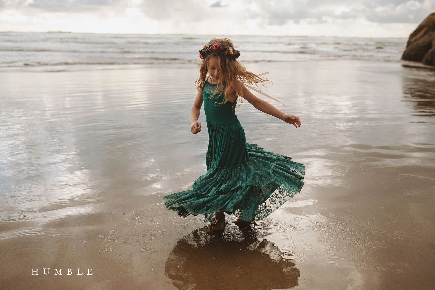 Person in a flowing dress dancing gracefully in shallow ocean waves.