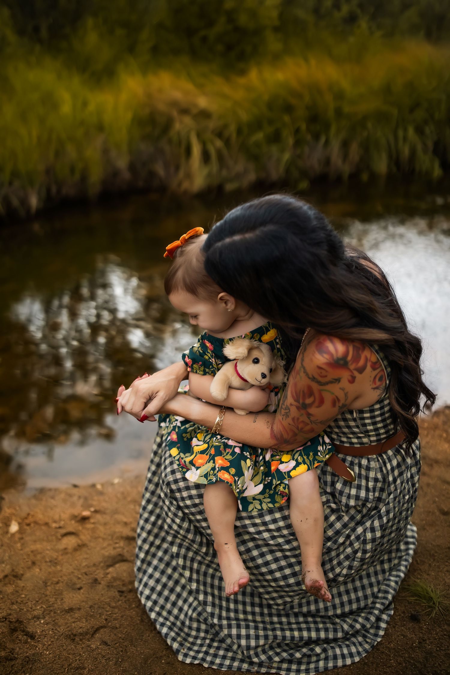 A tender moment captured by a lake as a parent embraces a small child wearing floral clothing.