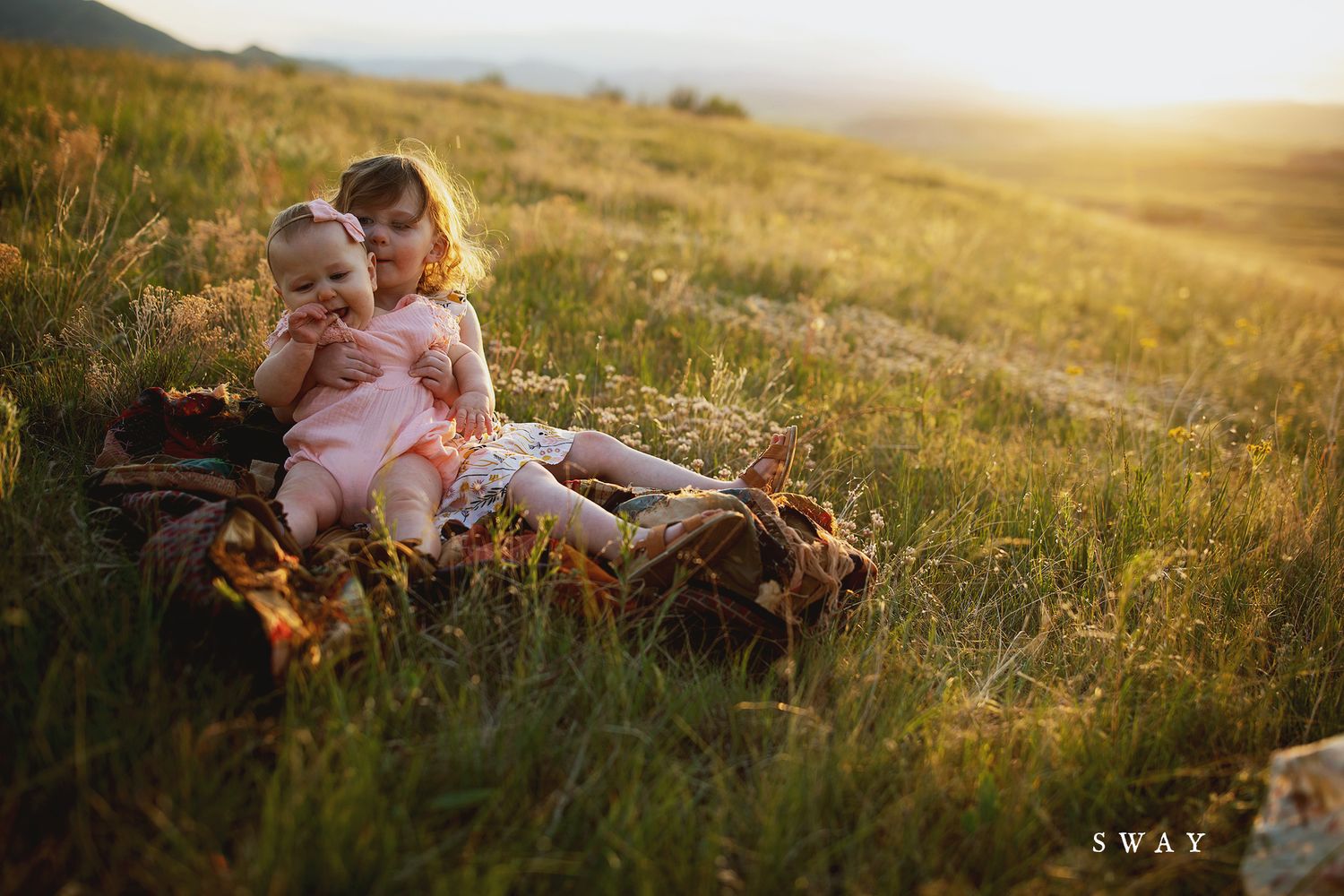 Candid family moment captured in warm evening light on grassy hillside.