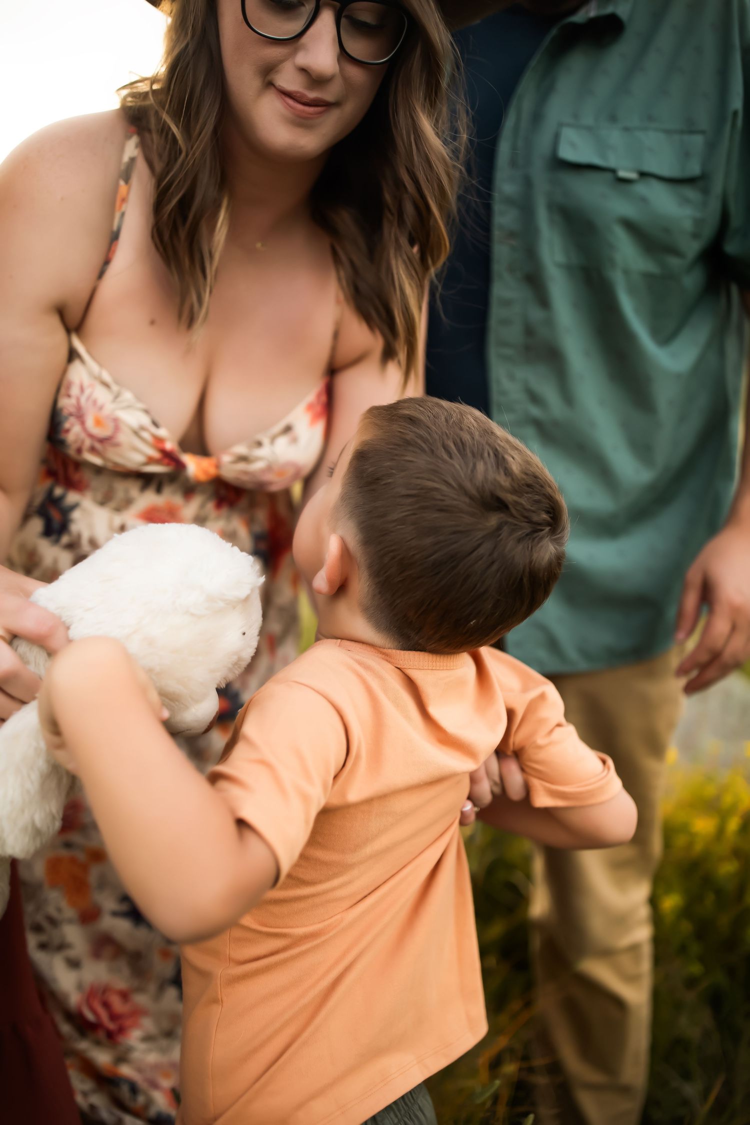 A child in an orange shirt embraces someone wearing a floral dress in an outdoor setting.