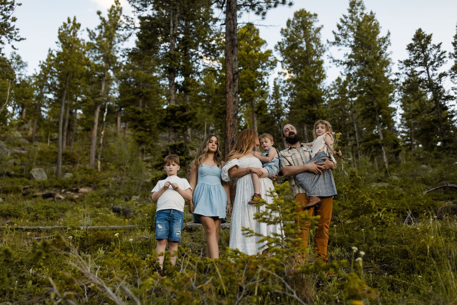 People stand together on a forested hillside during a gathering in a pine tree forest.