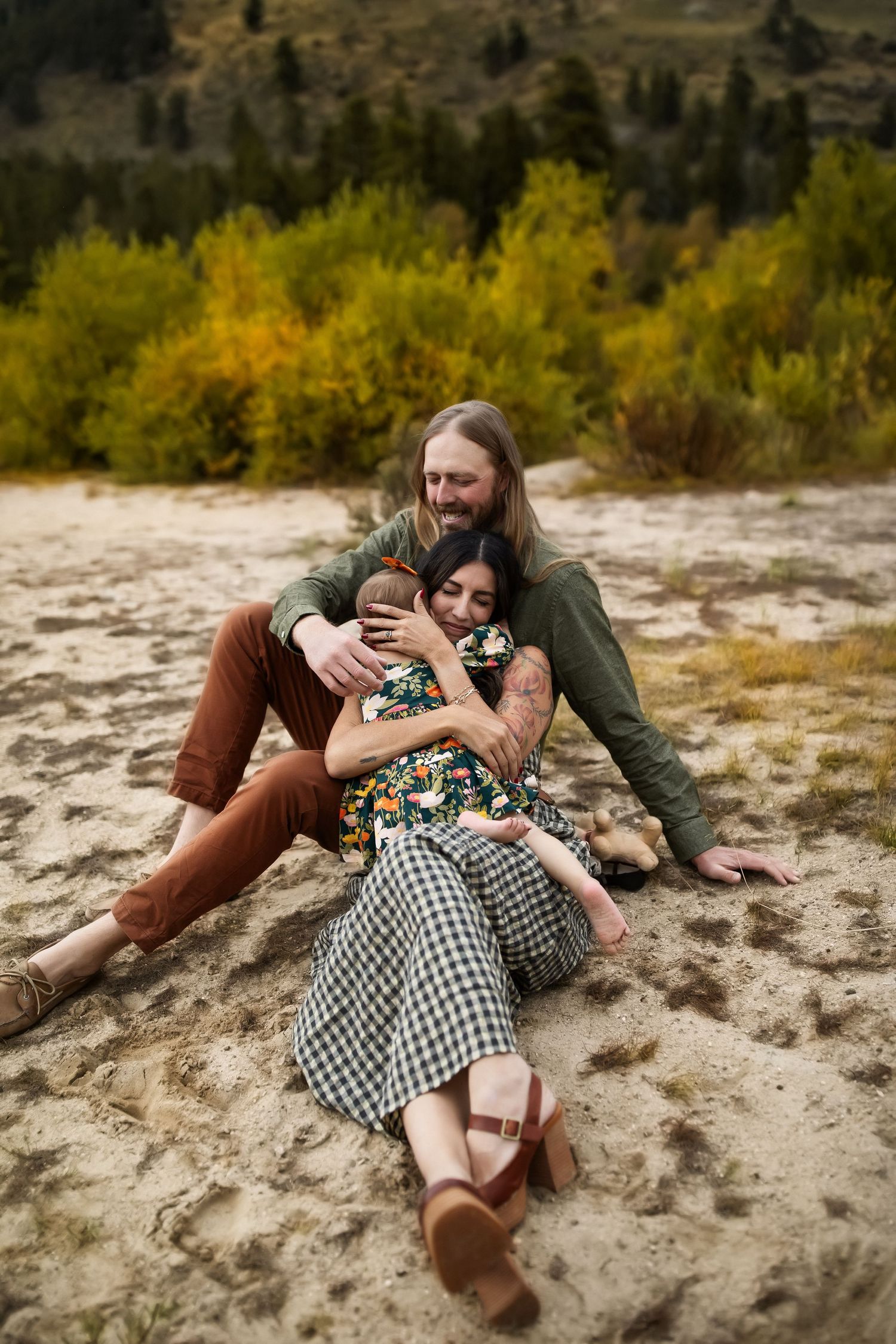 A romantic couple lying together on sandy ground surrounded by autumn foliage in a natural outdoor setting.