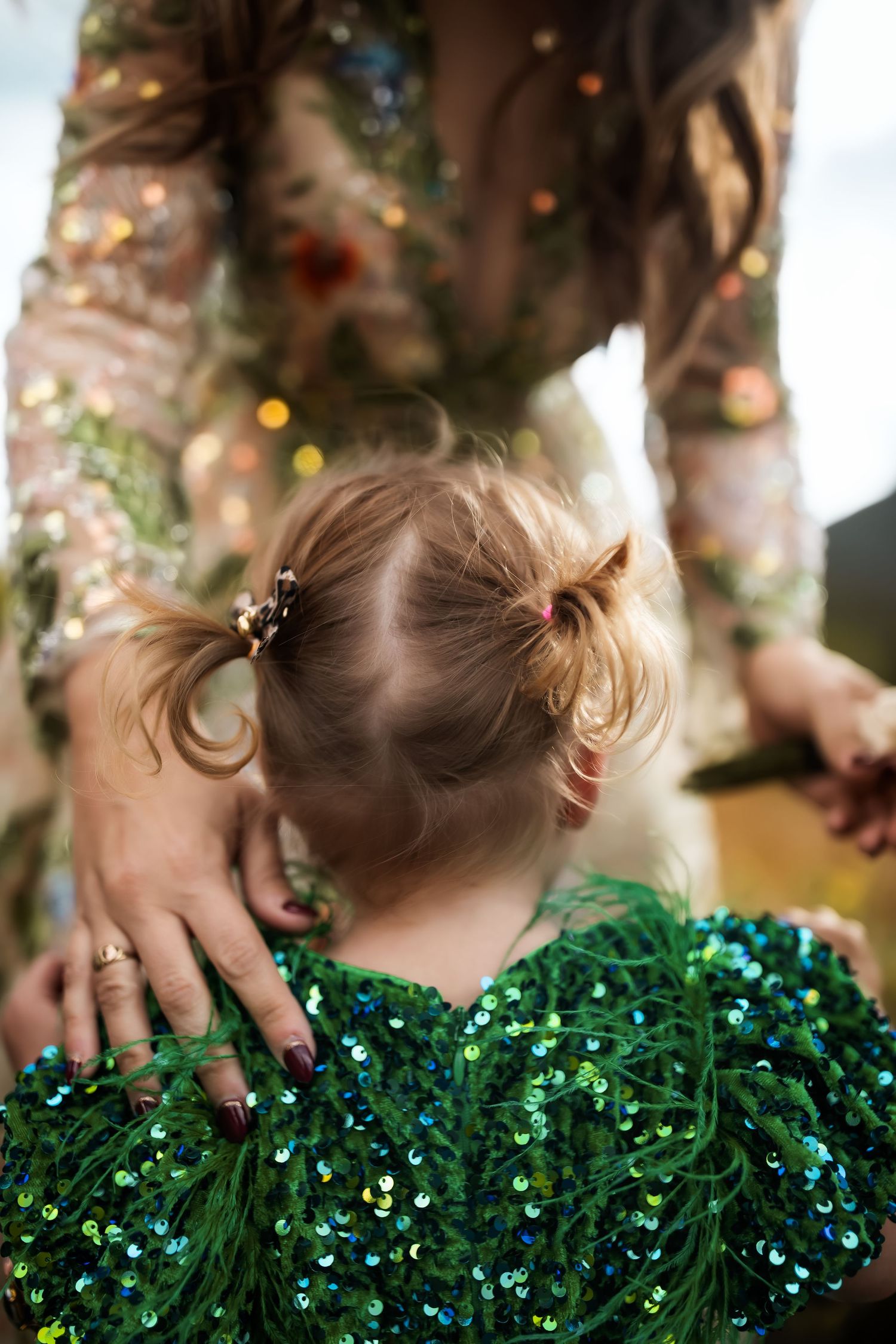A child's hands touch sparkly green tinsel garland decorations against a soft bokeh background.
