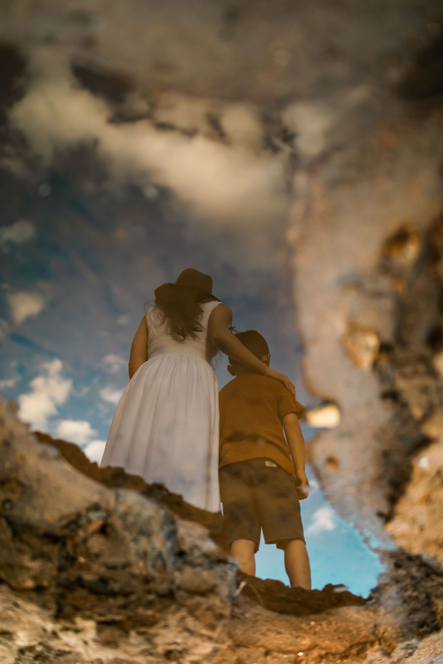 Dramatic reflection in a puddle shows silhouettes against a moody cloudy sky during golden hour.