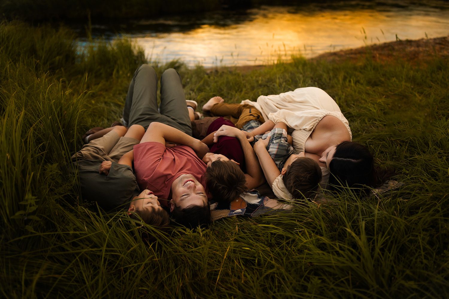People lying together in grass near a lake at sunset creating a dreamy summer scene.