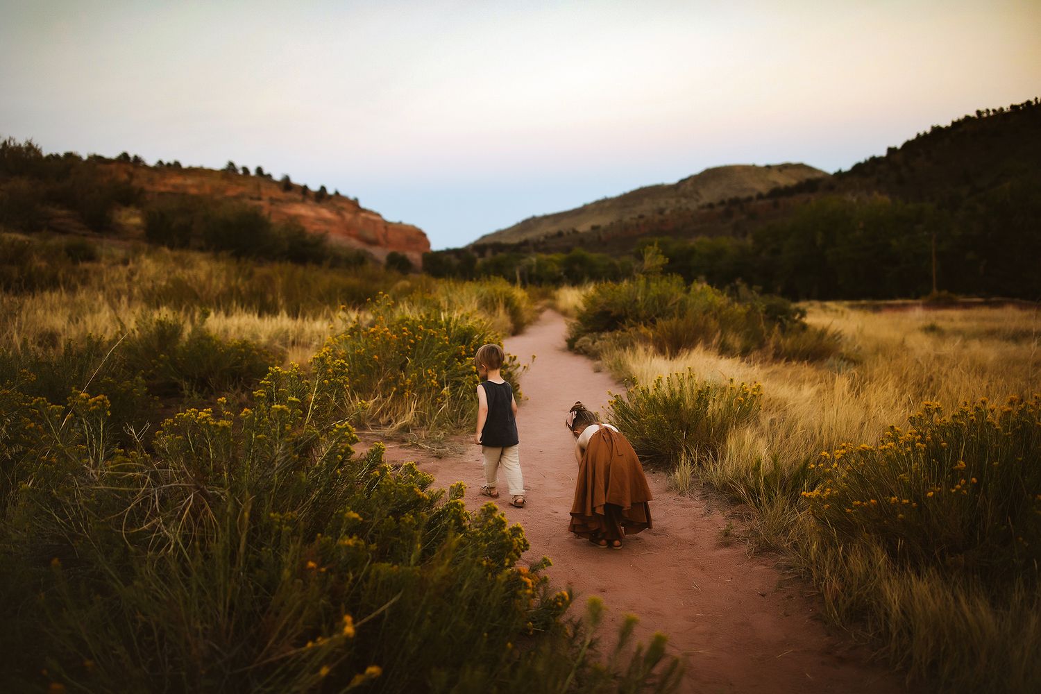 People walking along a dusty trail through golden mountain grasslands at sunset.