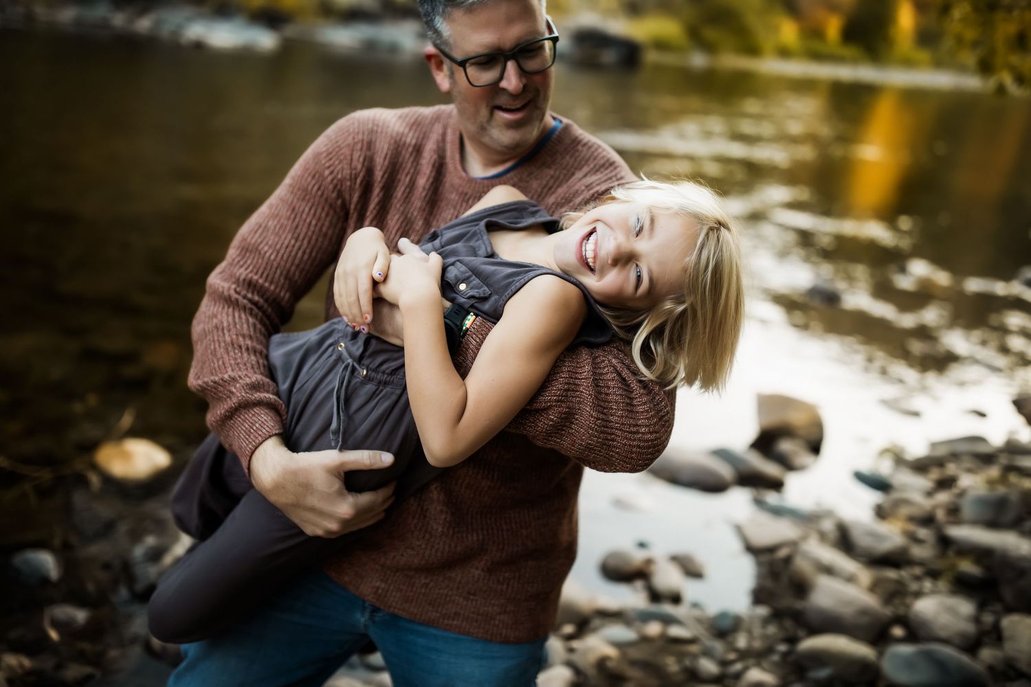 A playful moment captured by a rocky stream as a parent holds a laughing child in their arms.