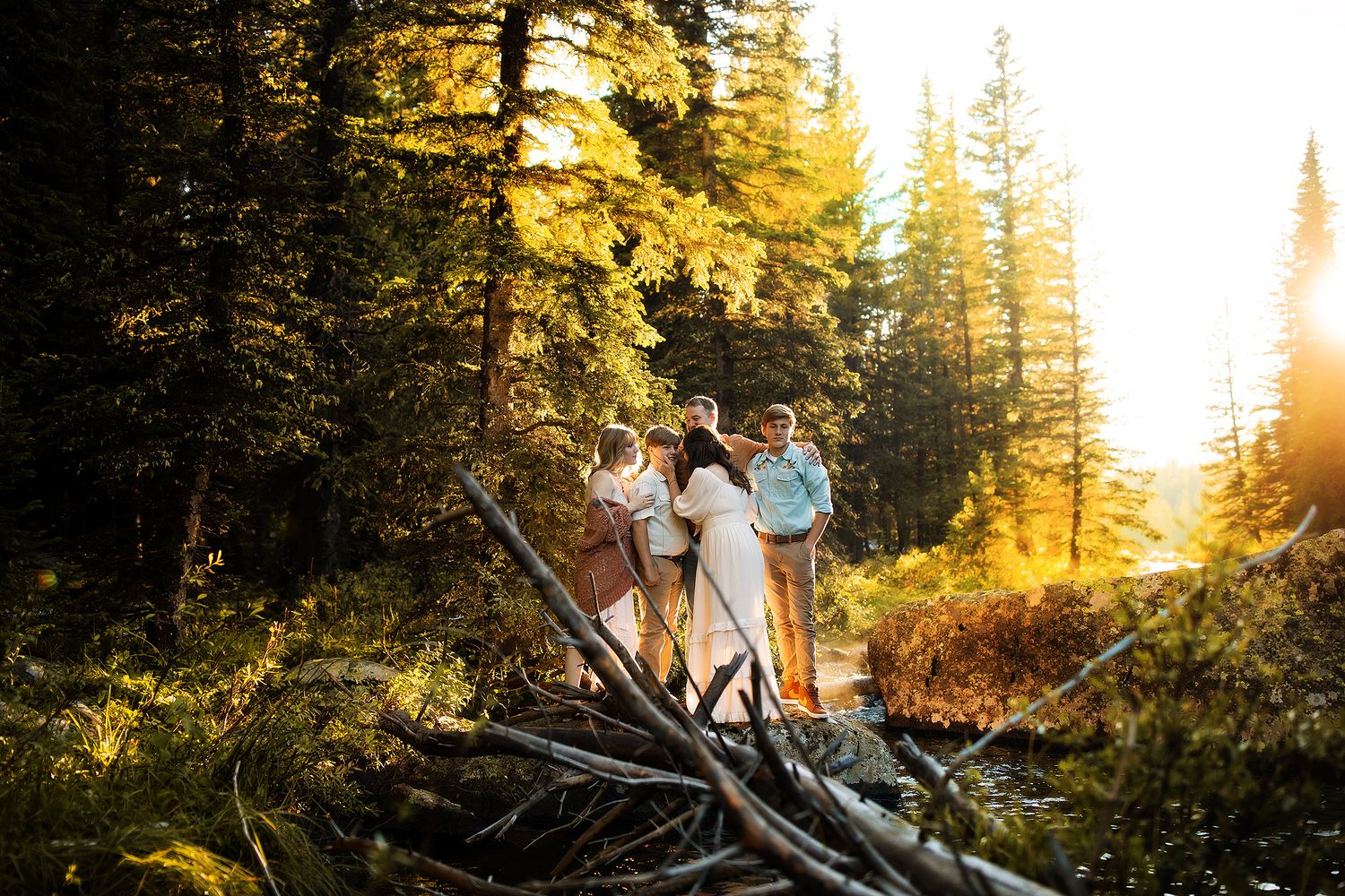 A group of people sit on fallen logs in a golden sunlit forest during sunset, creating a warm autumn atmosphere.