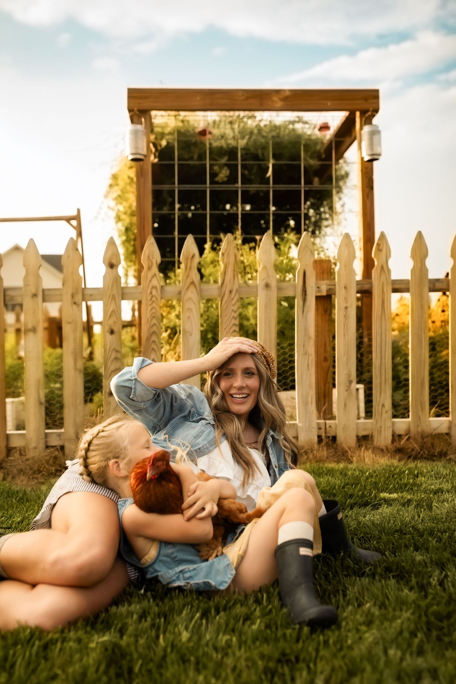 People relaxing on grass near a white picket fence during sunset.