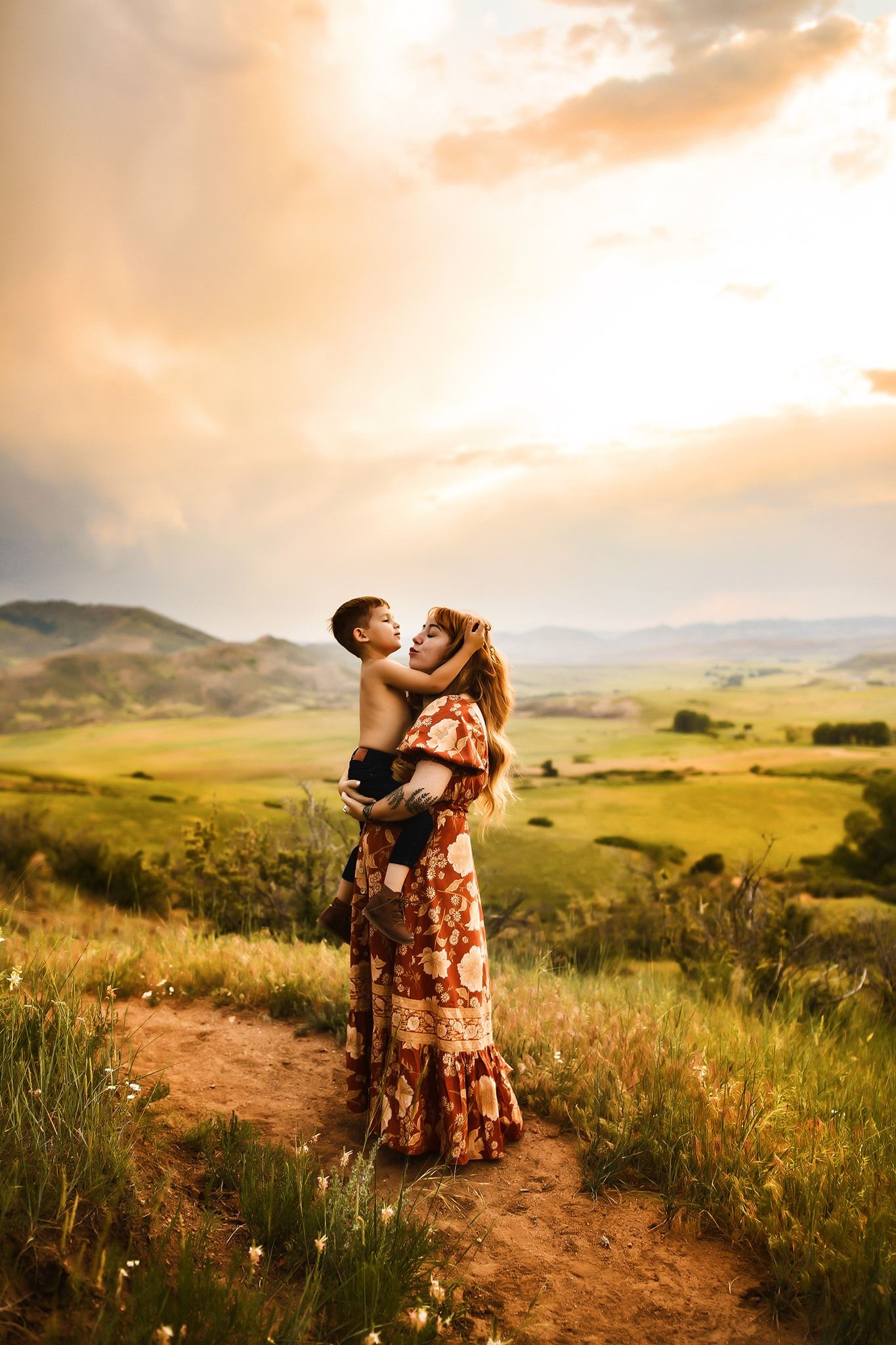 Couple embracing on hilltop trail during golden sunset in mountainous landscape.