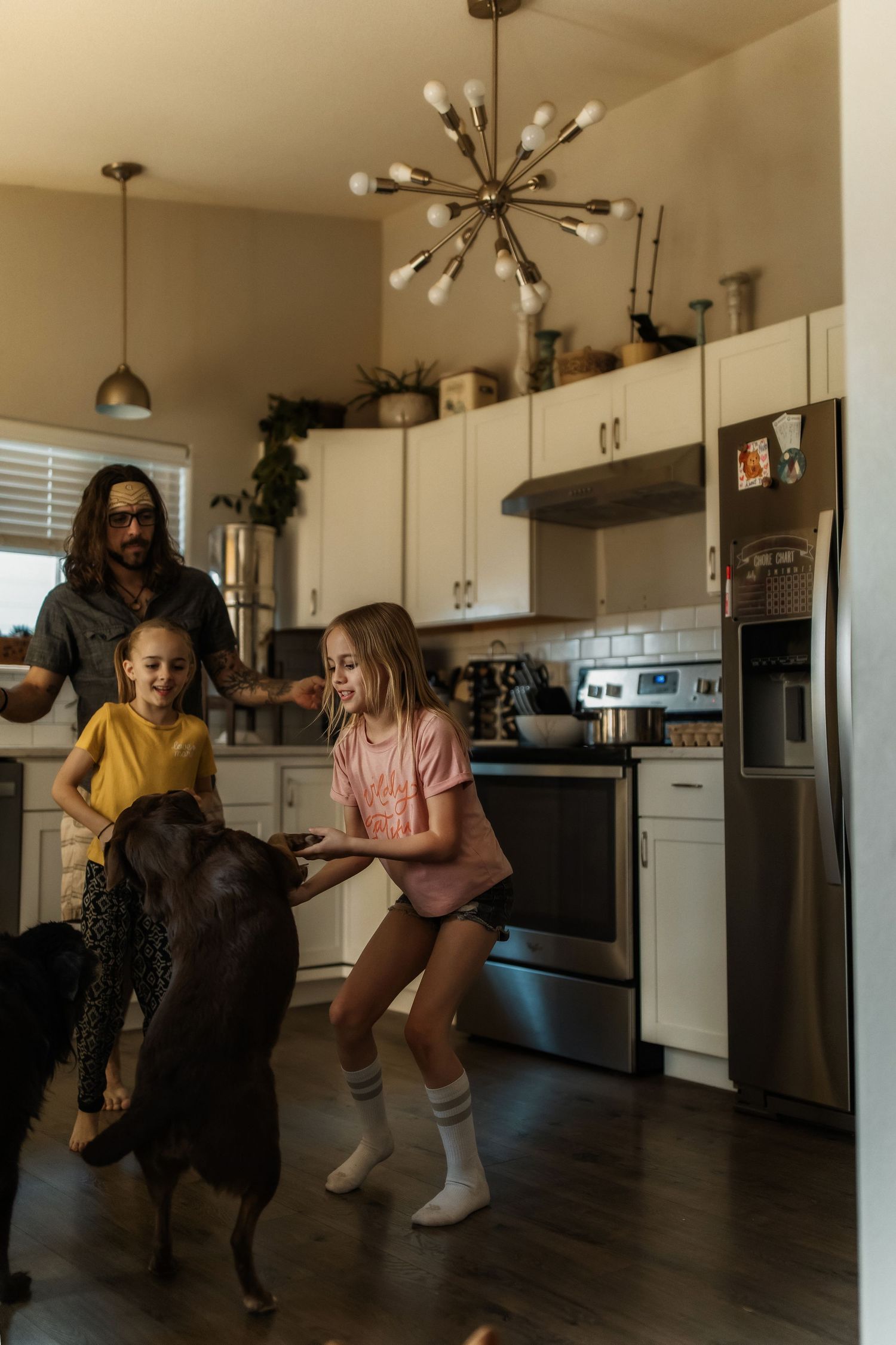 A family with two girls and a man interact with a chocolate Labrador in a modern kitchen with stainless steel appliances.
